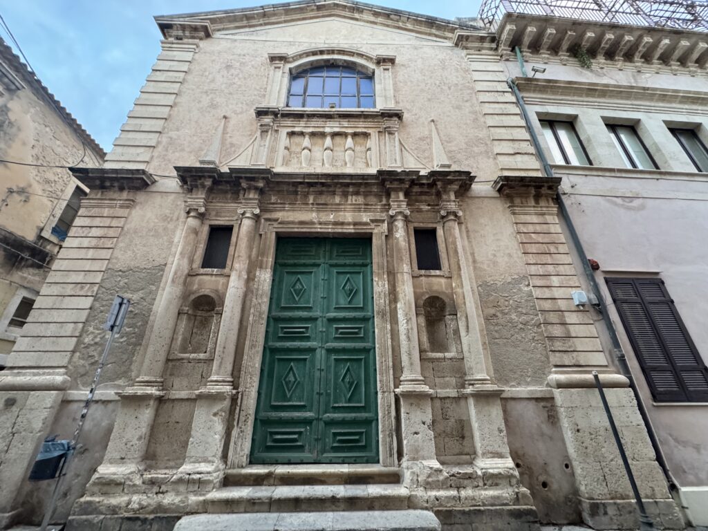 Facciata della Chiesa di San Benedetto a Siracusa, con portale verde centrale e colonne ai lati.