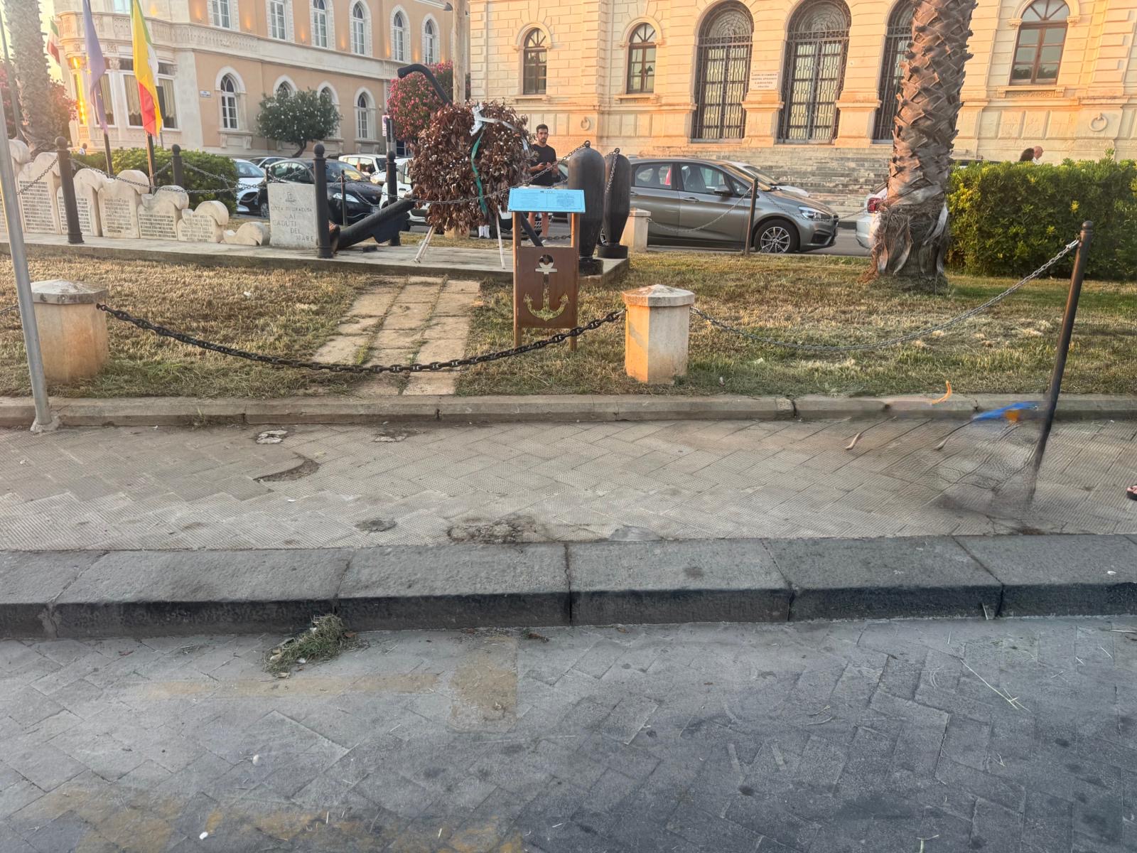 Scalino senza rampa che separa il marciapiede con il Monumento ai Caduti del Mare dal livello stradale.