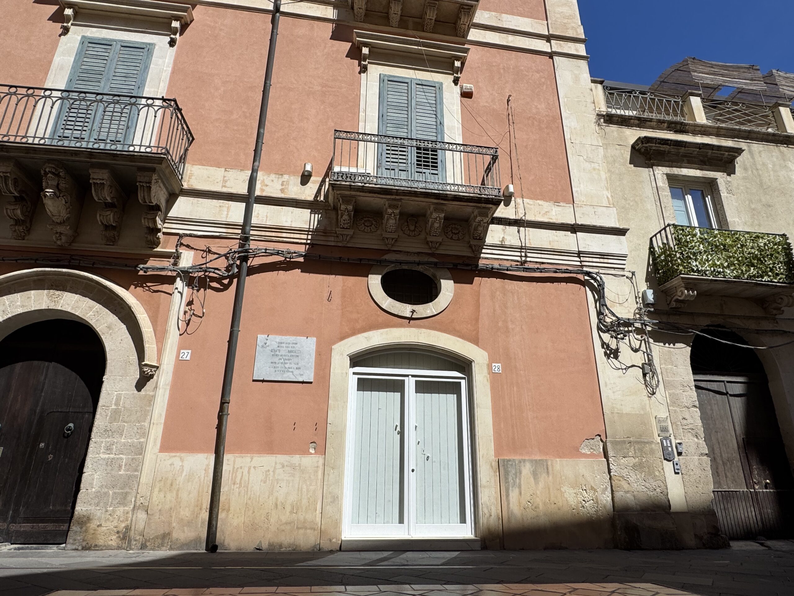 Facciata di Palazzo Randazzo in piazza San Giuseppe a Siracusa, con la lapide marmorea dedicata a Renato Randazzo tra i civici 27 e 28.