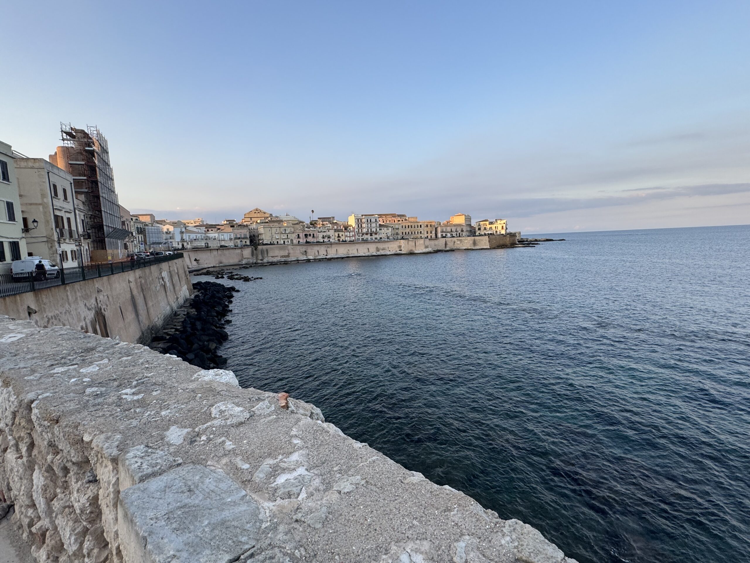 Panorama del fronte urbano di Ortigia visto dall’Affaccio Enzo Maiorca, con il muraglione in pietra in primo piano e il mare Ionio che si apre sulla destra.