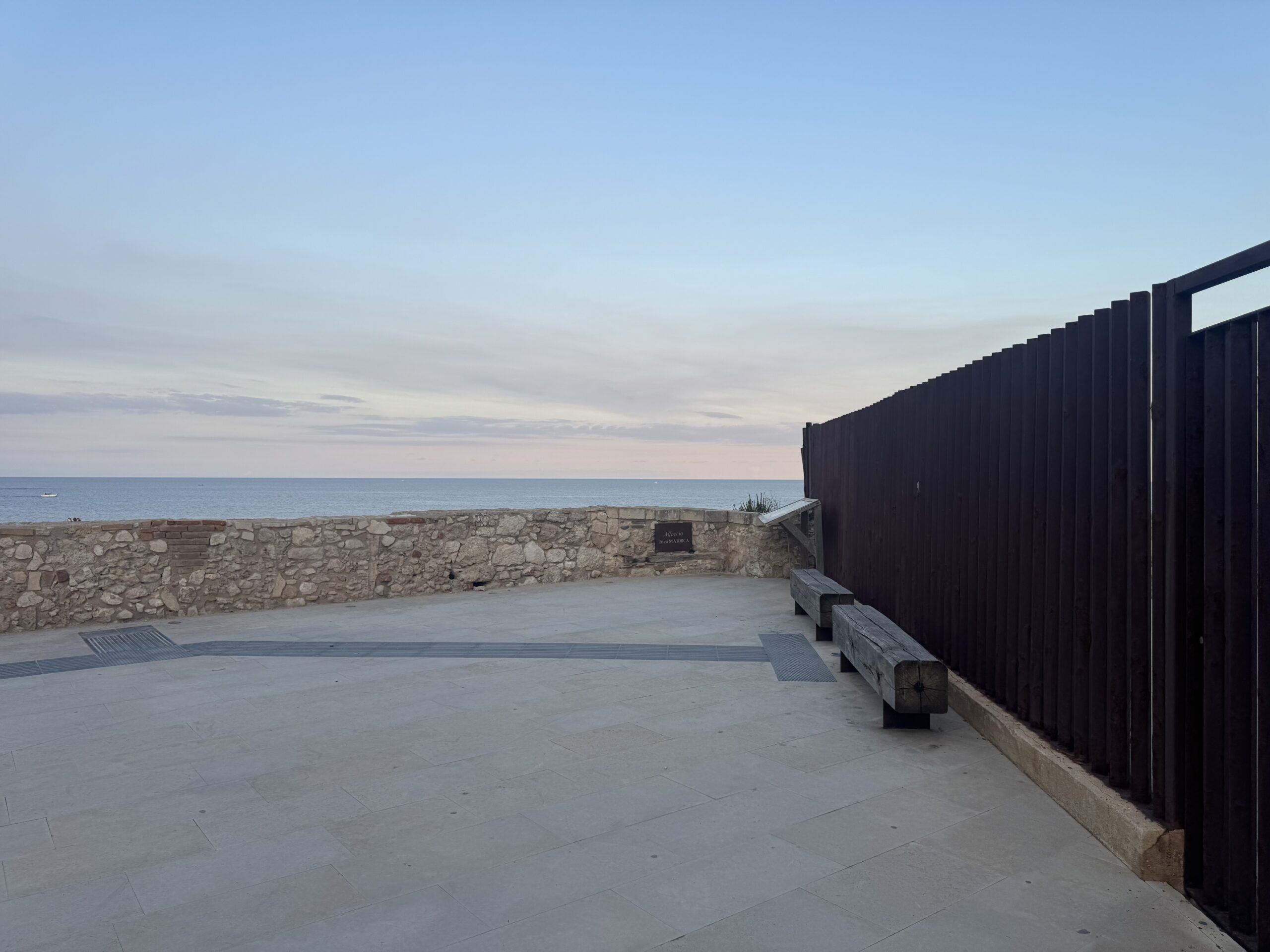 Affaccio Enzo Maiorca a Ortigia, con lo slargo pavimentato, le panchine in legno rivolte verso il mare e la targa dedicata all’apneista sul muretto di pietra.