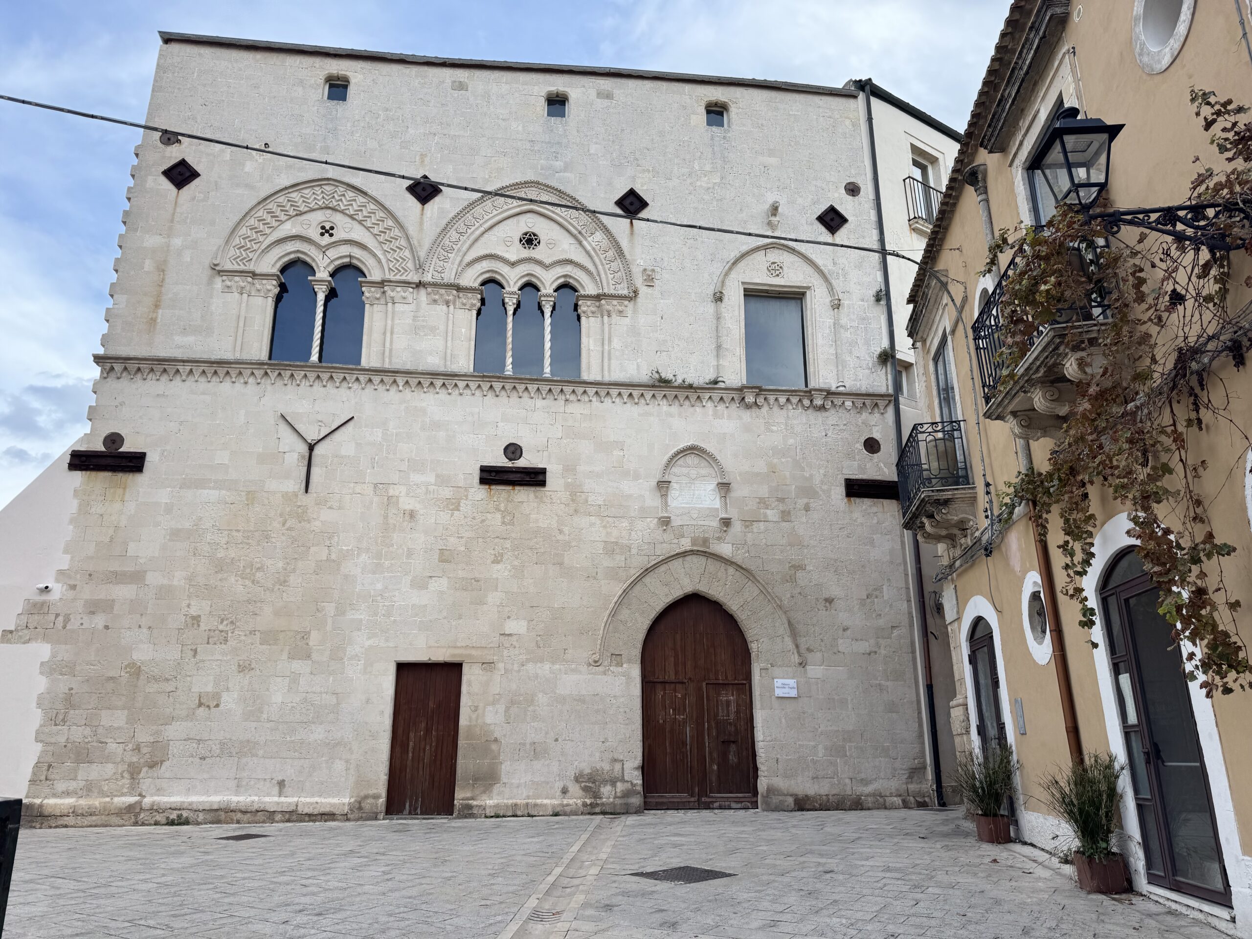 Facciata principale di Palazzo Montalto in pietra calcarea: al piano terra portale ogivale e porta minore; al piano nobile bifora e trifora con colonnine e cornici scolpite, più una monofora laterale; marcapiano dentellato e rosoni traforati.