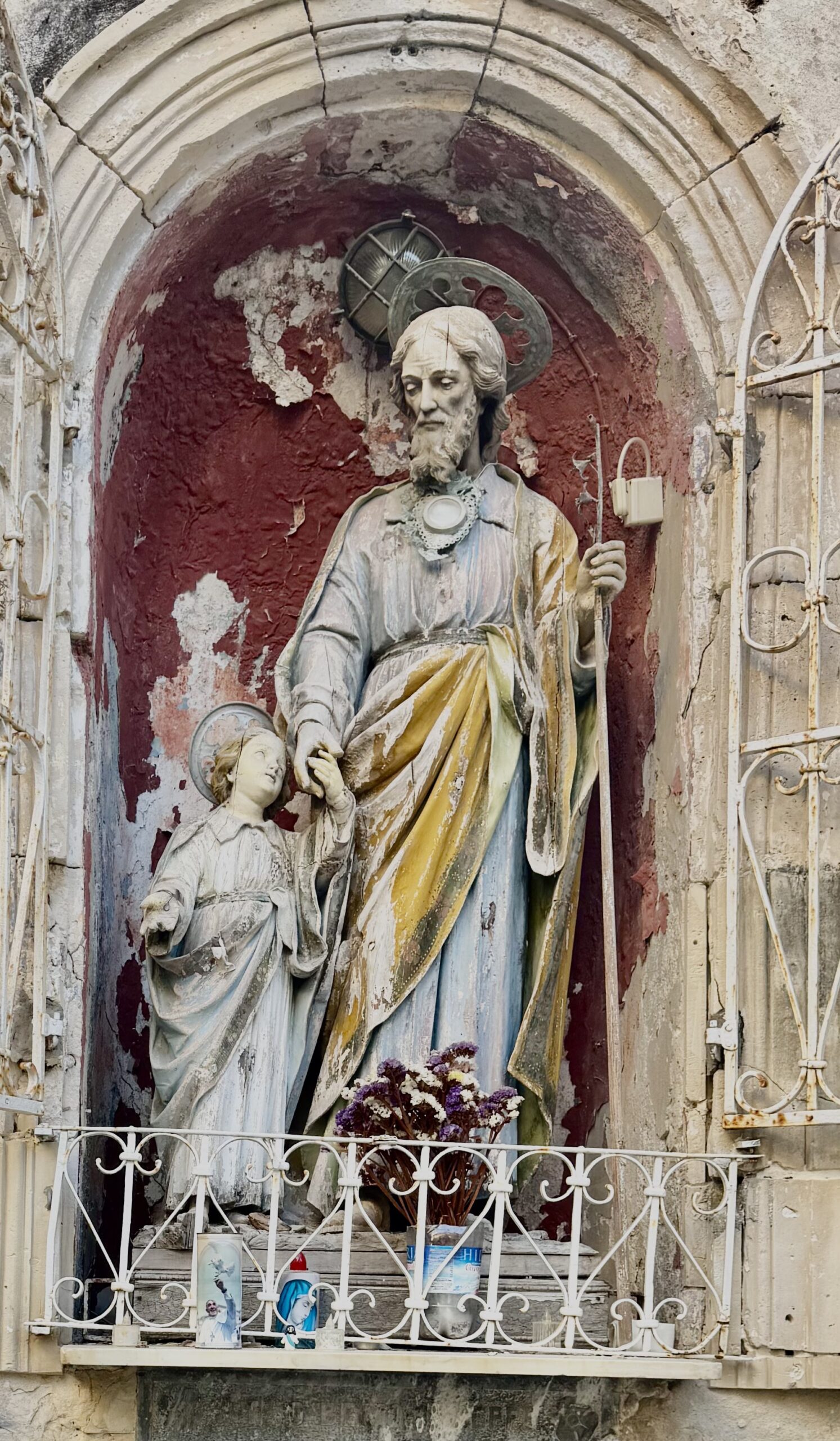Dettaglio ravvicinato della statua di San Giuseppe col Bambino Gesù: si distinguono le vesti policrome deteriorate, l'aureola metallica e il bastone fiorito