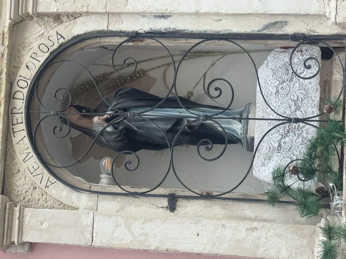 Dettaglio della statua della Mater Dolorosa avvolta in manto nero, dietro il cancelletto in ferro battuto decorato con volute, nell'edicola votiva di Vicolo delle Pergole a Ortigia