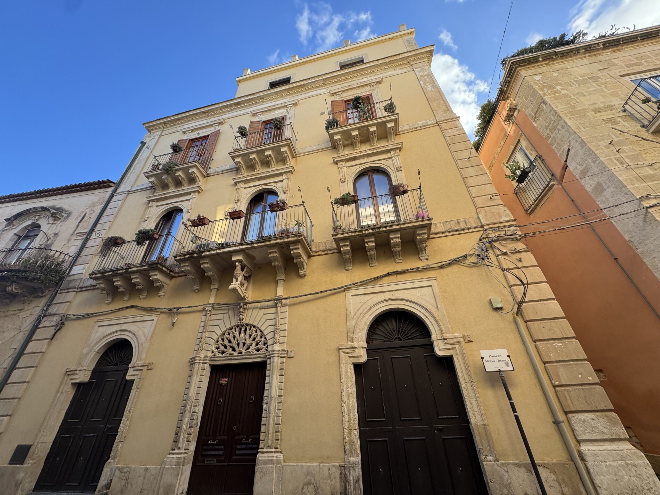 Facciata a tre ordini del Palazzo Mezio-Blanco in Via Vittorio Veneto a Ortigia, con i tre portali arcuati, il mensolone a grifone e la merlatura decorativa
