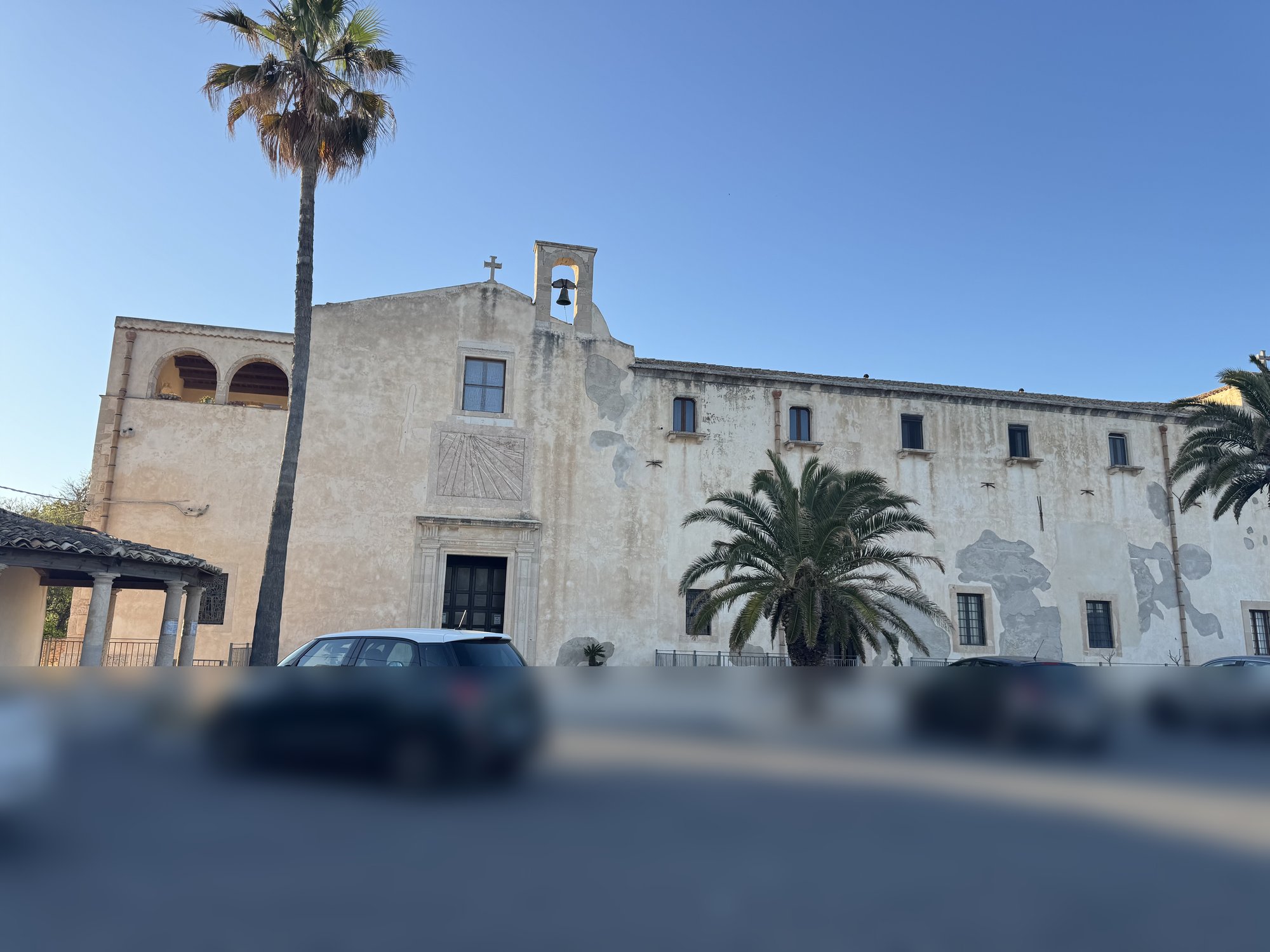 Vista panoramica del lato lungo del complesso conventuale dei Cappuccini di Siracusa, con la facciata della chiesa al centro, il campanile a vela, la meridiana sopra il portale, la loggia spagnola sulla sinistra e gli edifici del convento sulla destra