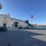 Vista d'insieme della piazza Cappuccini di Siracusa con il complesso conventuale sulla sinistra, la pavimentazione in lastre di basalto a chiocciola, palme e cielo terso al pomeriggio