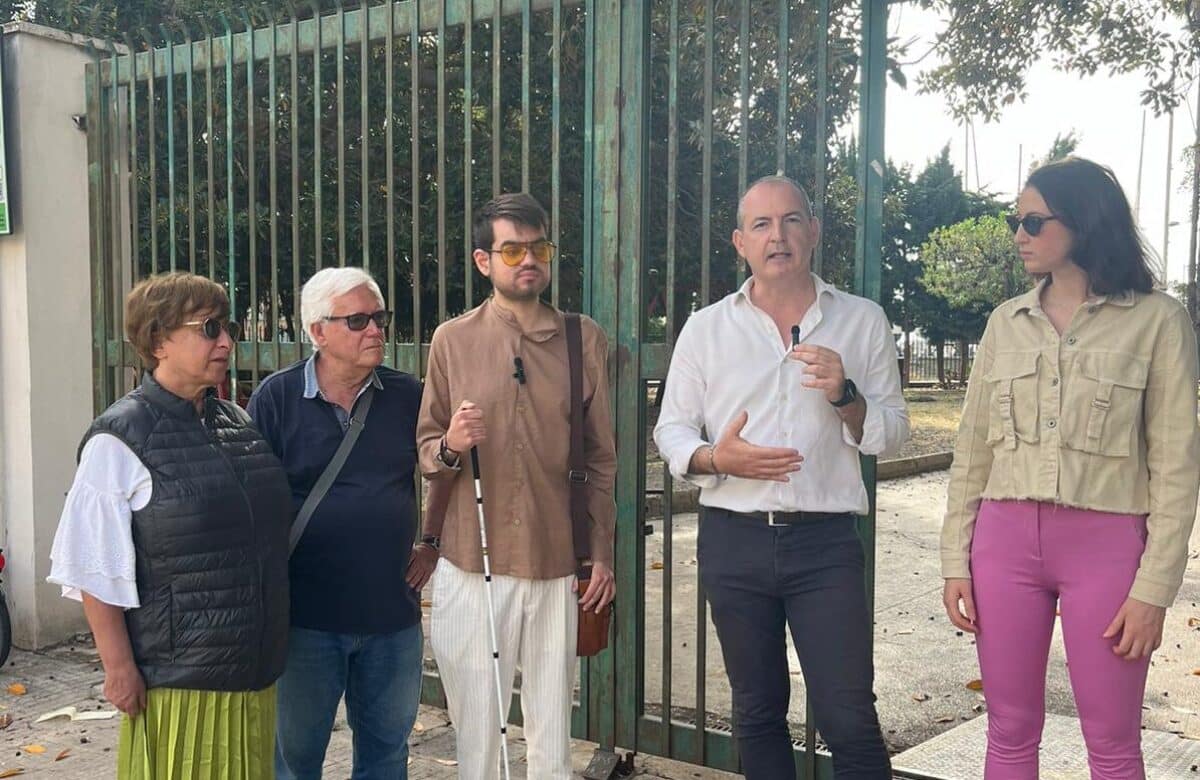 Cinque persone in piedi davanti a un cancello verde all'aperto.