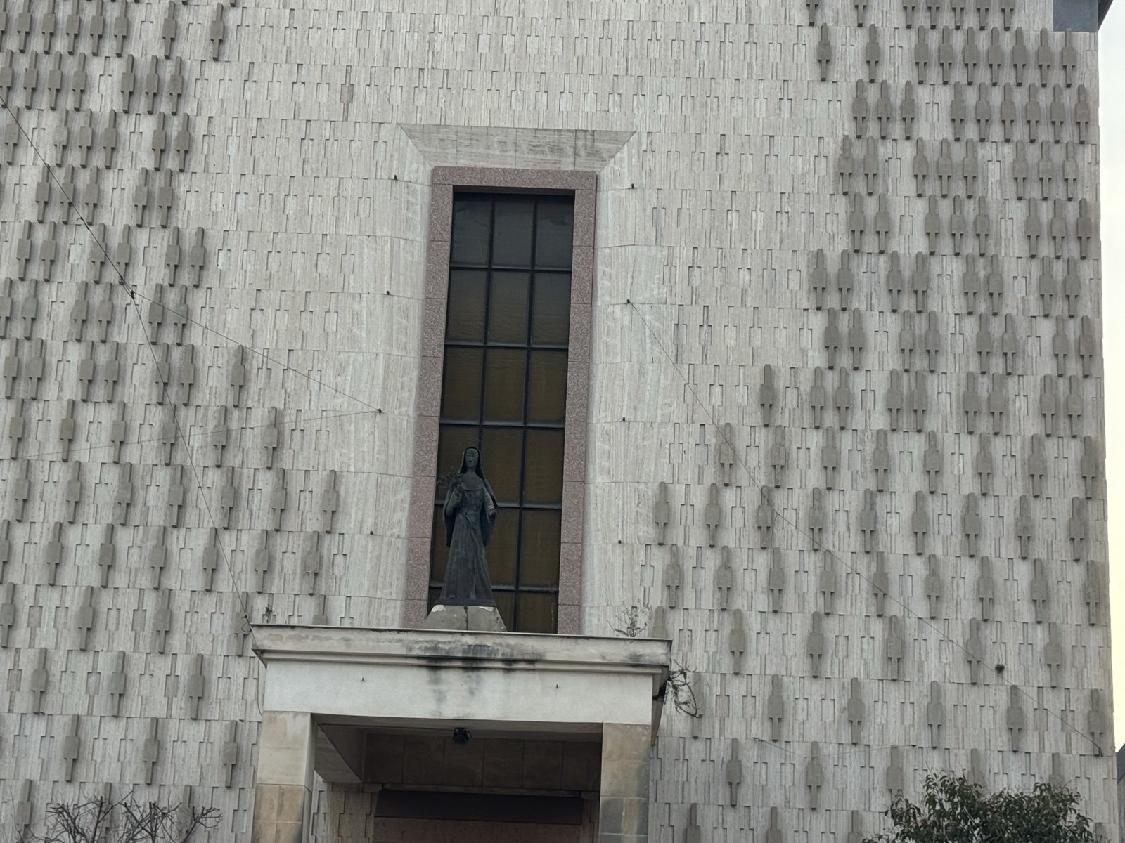 Dettaglio della facciata della Chiesa di Santa Rita di Siracusa: statua bronzea della santa in nicchia sopra il portale e grande finestra verticale