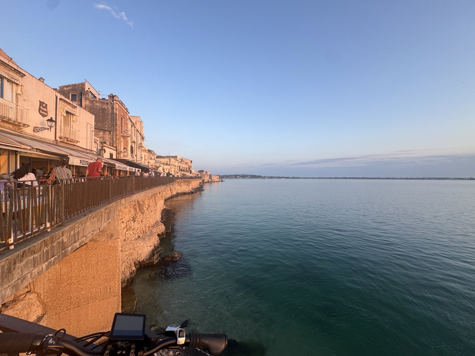 Lungomare Alfeo dal lato meridionale: marciapiede a sbalzo sopra il muraglione di pietra che incorpora le antiche fortificazioni, con bicicletta in primo piano