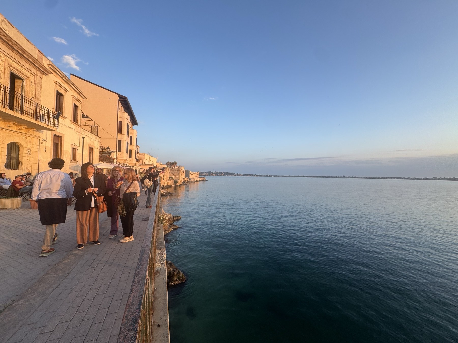 Passeggiata serale sul Lungomare Alfeo a Ortigia con persone, edifici storici, balaustra e mare al tramonto