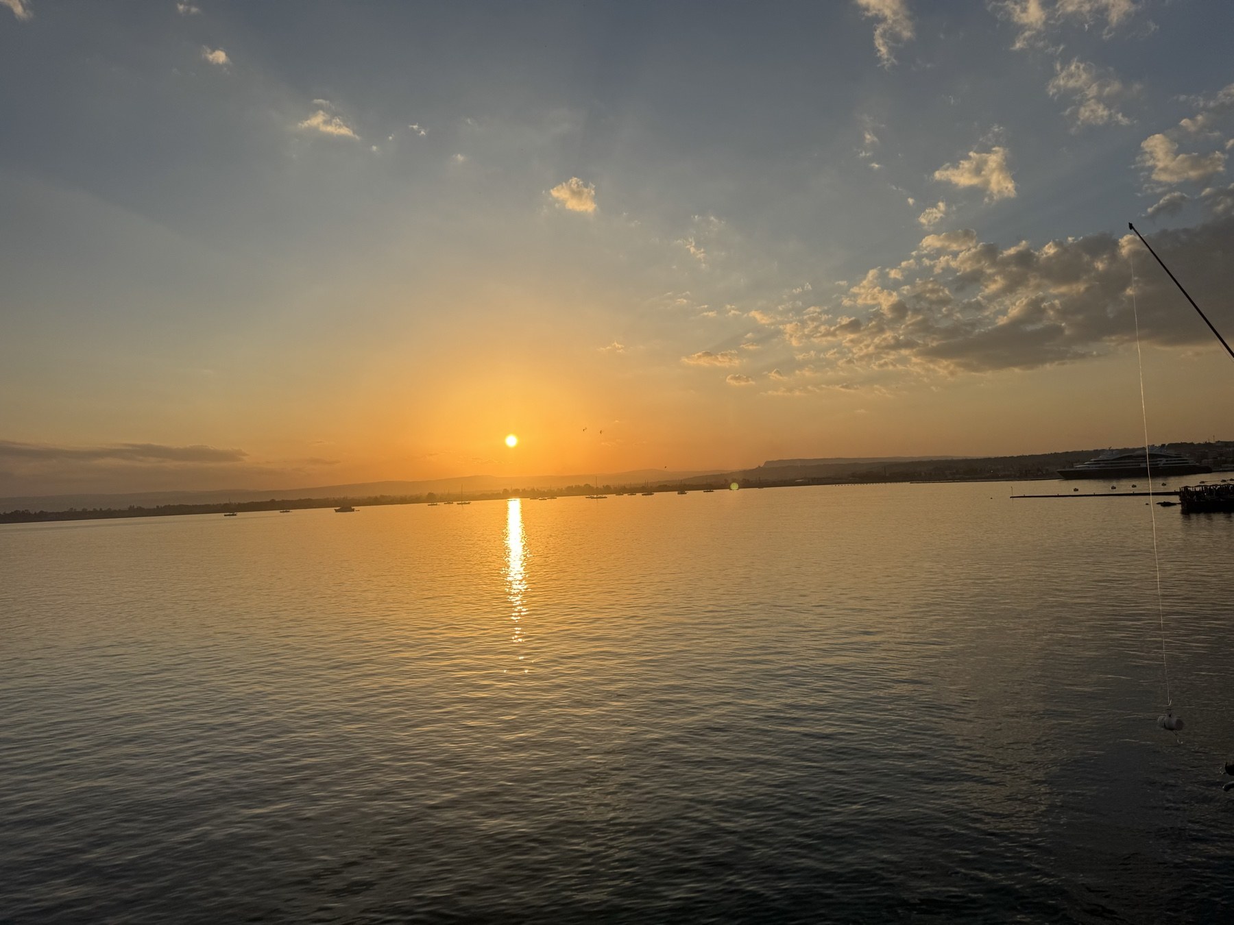 Tramonto sul Porto Grande visto dal Lungomare Alfeo a Ortigia, con sole basso sull'orizzonte e riflessi dorati sul mare