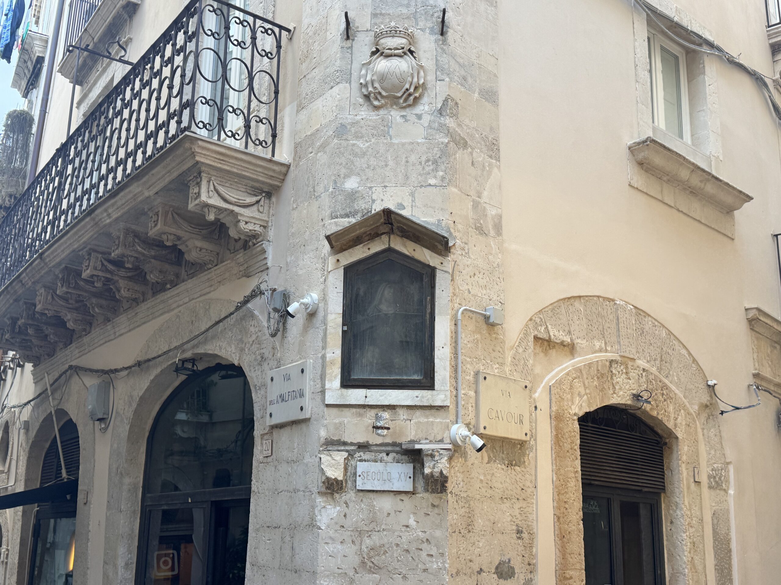 Dettaglio dell'edicola votiva della Madonna della Pietà con timpano, stemma nobiliare e nicchia scura contenente l'immagine sacra