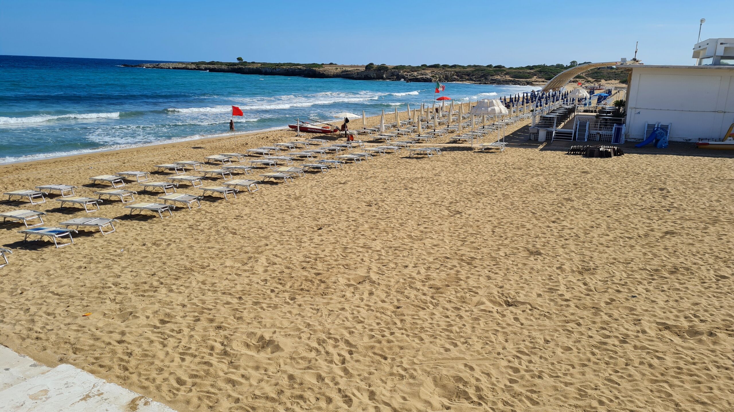 Spiaggia sabbiosa con lettini e mare azzurro.