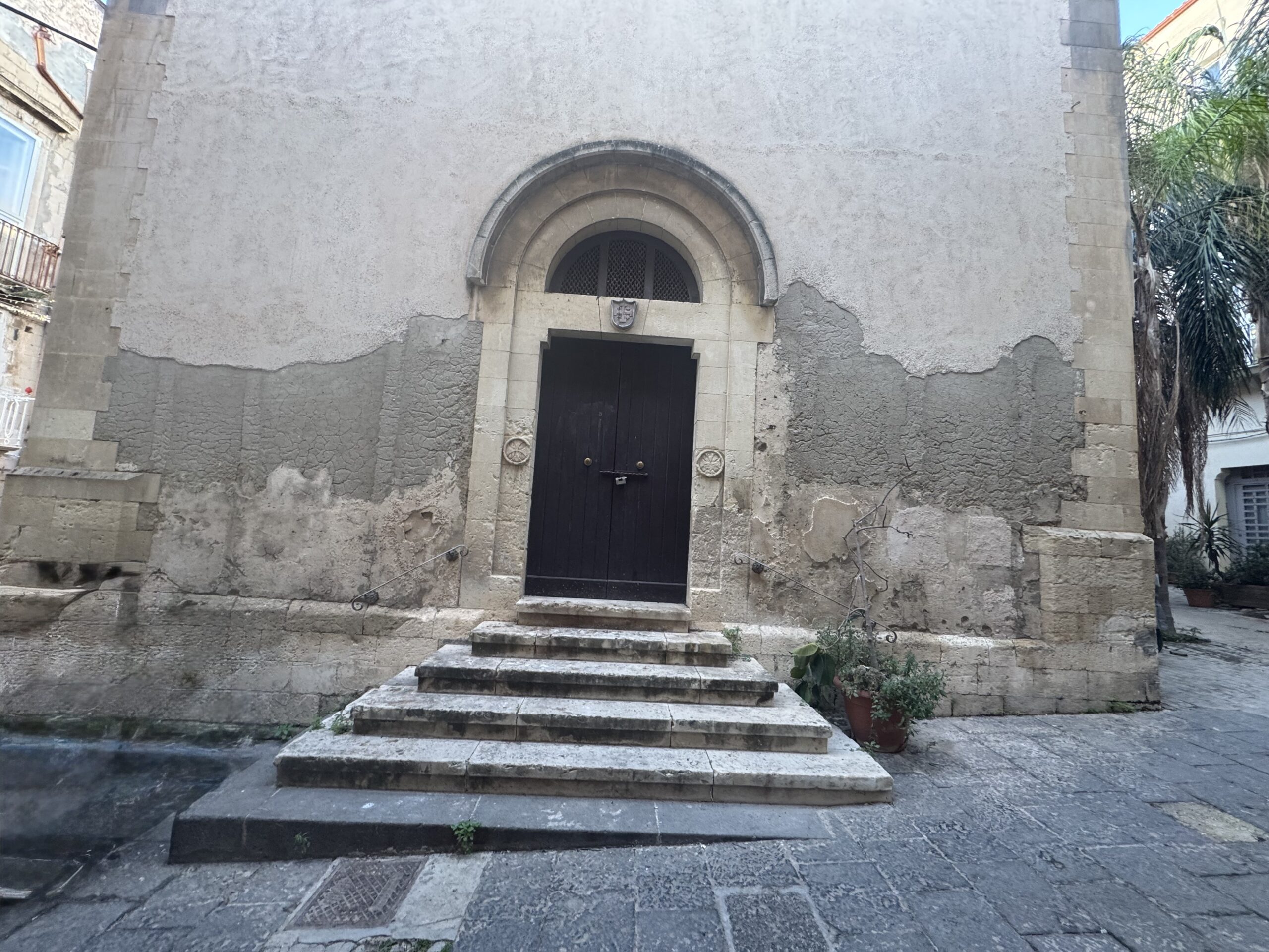 Prospetto frontale della Chiesa di San Tommaso ad Ortigia, con portale ad arco a tutto sesto, doppio battente in legno scuro e quattro gradini di accesso in pietra calcarea.