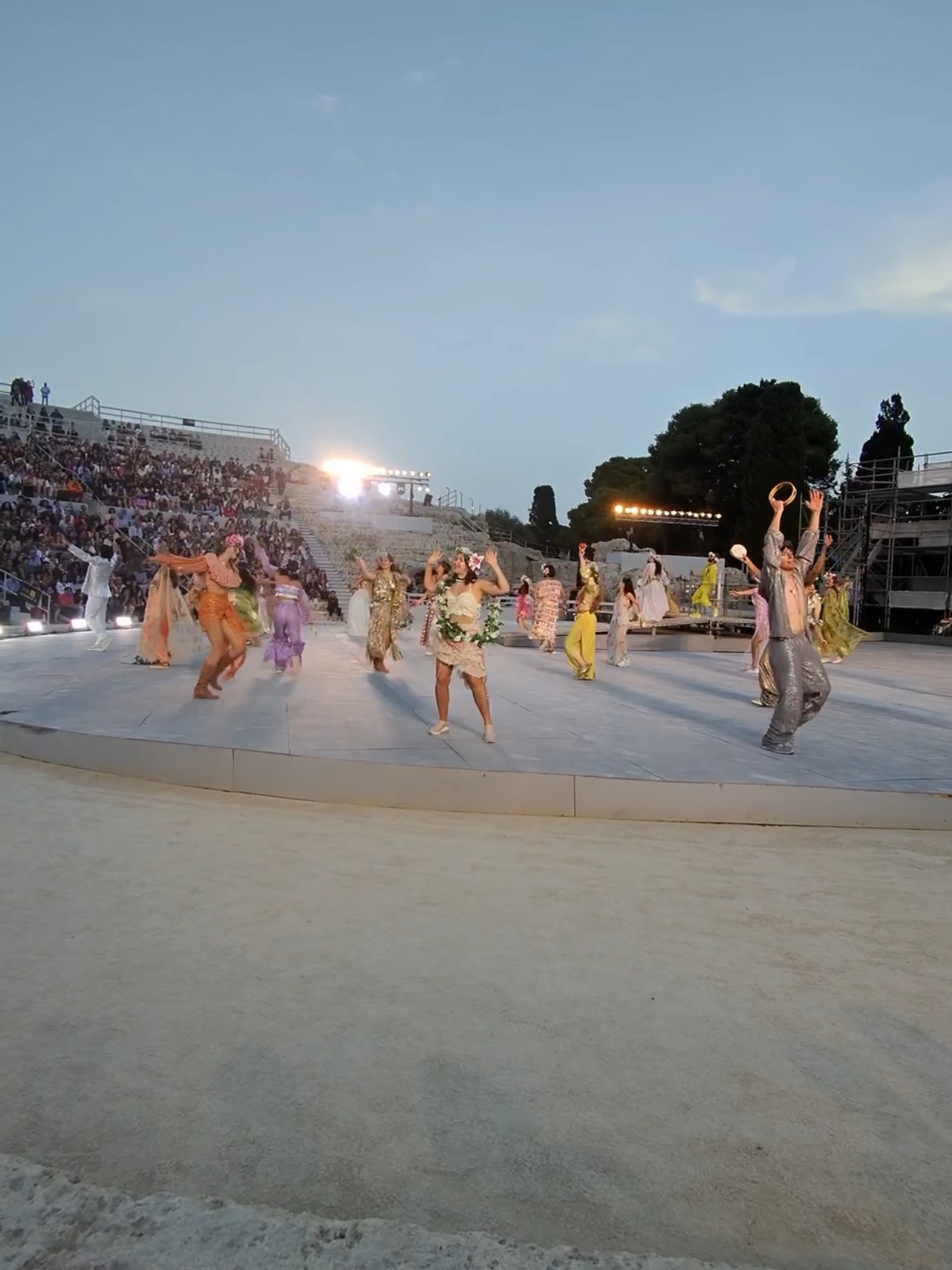 Coro e danzatori in scena al Teatro Greco di Siracusa durante una rappresentazione INDA, con cavea al tramonto