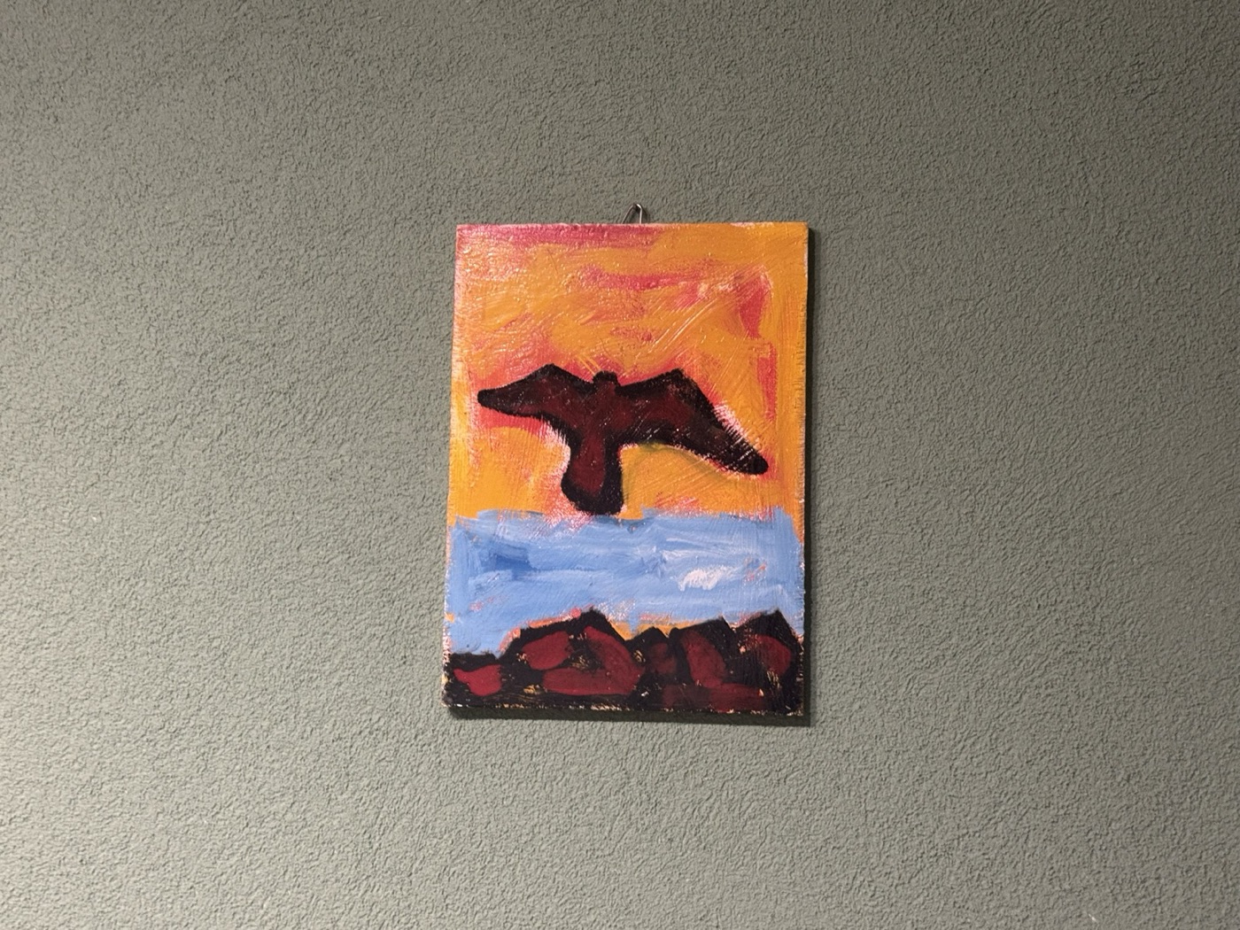 Dipinto di Salvatore Accolla raffigurante un uccello in volo silhouette nera su cielo arancione, mare blu, scogli rossi