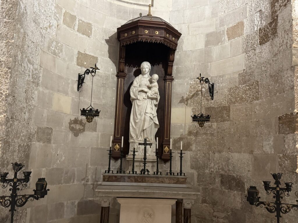 Vista frontale della statua marmorea della Madonna della Neve di Antonello Gagini (1512), opera capitale della scultura rinascimentale siciliana, custodita nell'apside bizantino-normanno del Duomo di Siracusa: Madonna con Bambino in piedi, sotto baldacchino ligneo dorato, lampade laterali in ferro battuto.