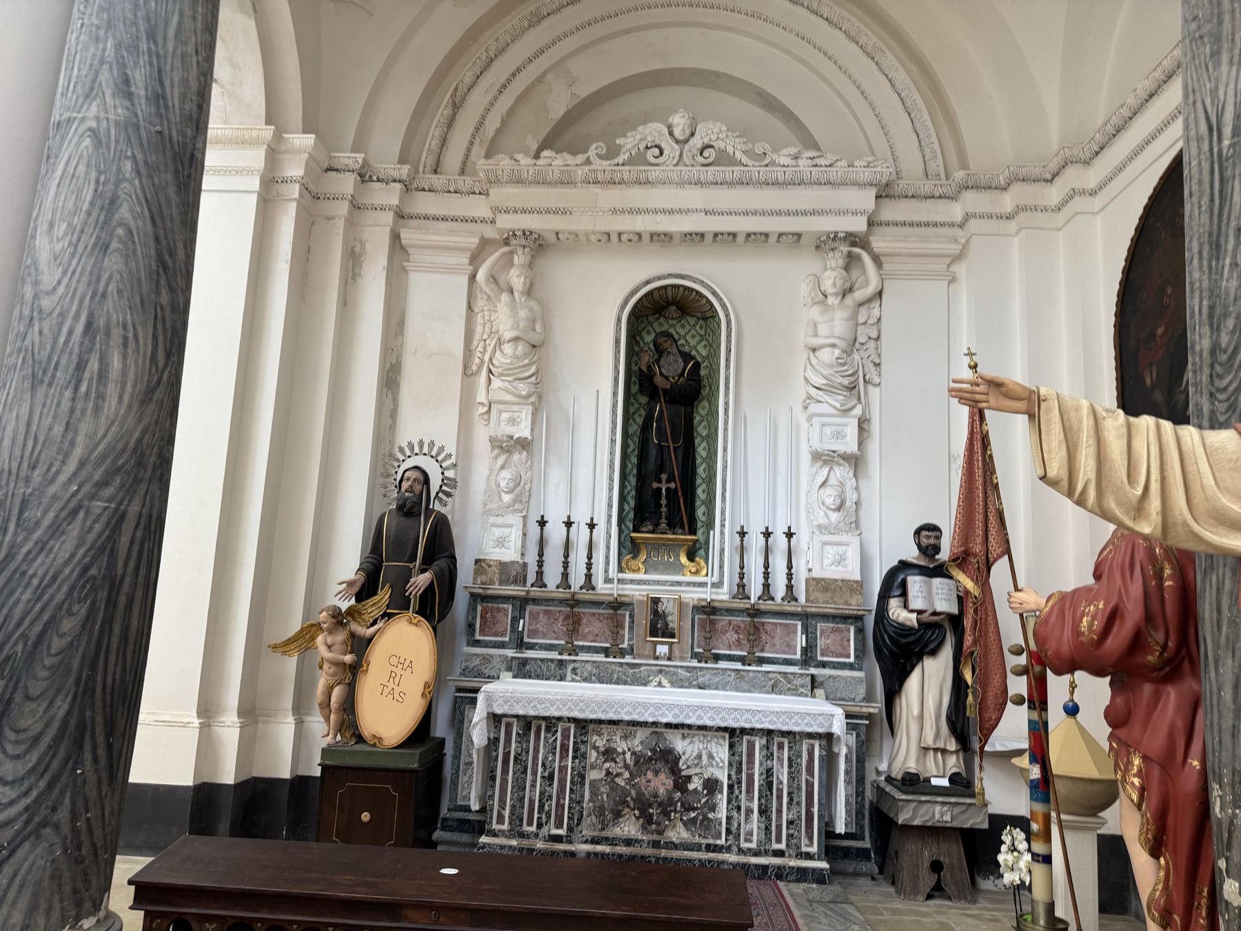 Altare laterale con nicchia e statua di un santo in saio scuro, affiancato da due telamoni in stucco bianco; davanti, il simulacro di San Francesco di Paola con il disco Charitas.