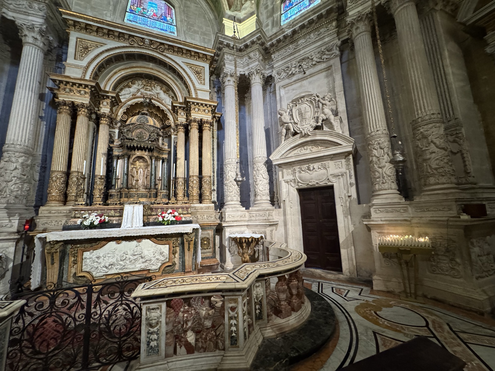 Altare maggiore con colonne corinzie e portale laterale con stemma vescovile e cherubini