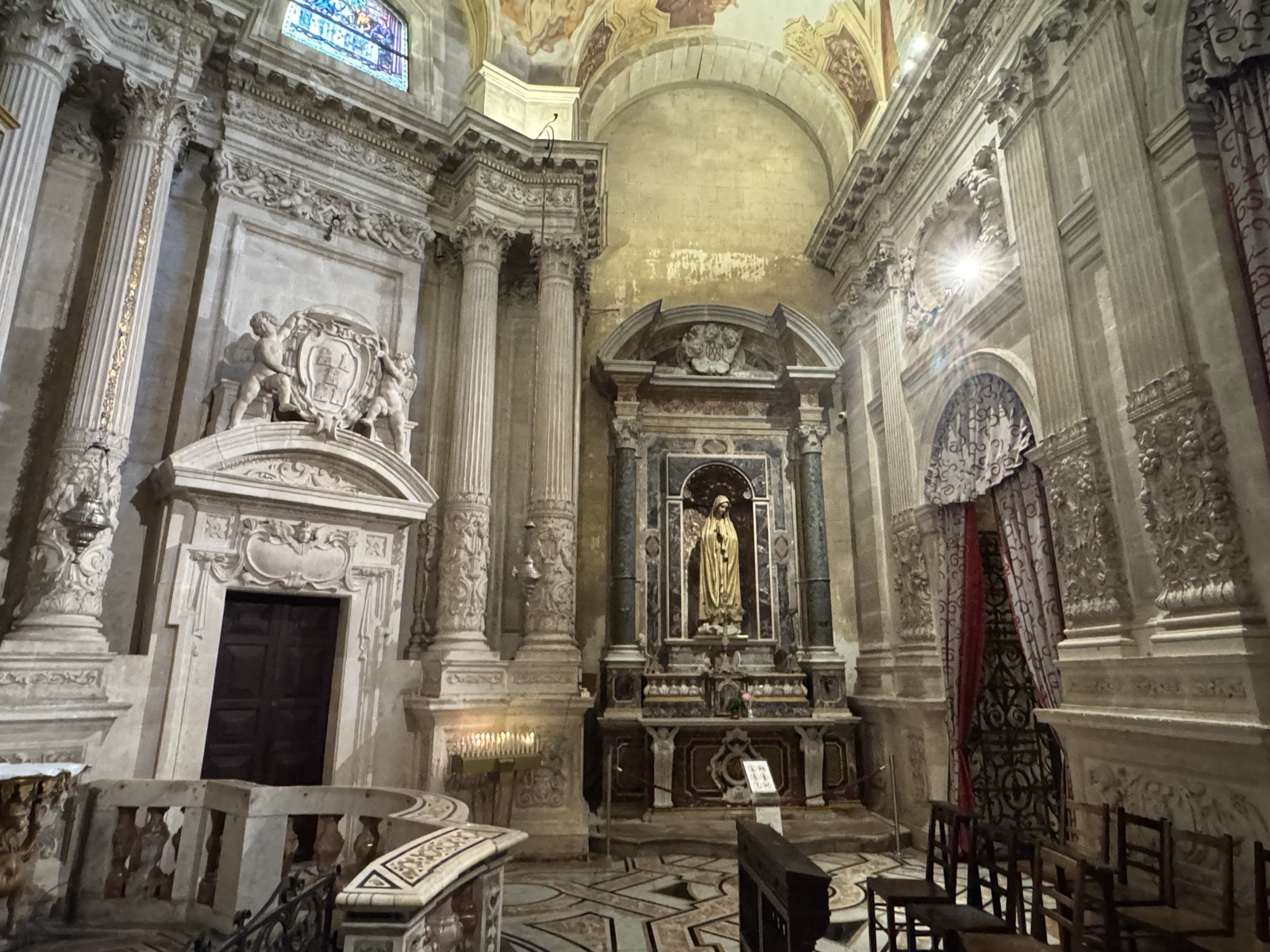 Edicola scolpita all'interno della Cappella del Santissimo Sacramento del Duomo di Siracusa con portale, cherubini e stemma vescovile in alto, statua marmorea della Vergine in nicchia centrale e cariatidi scolpite ai lati