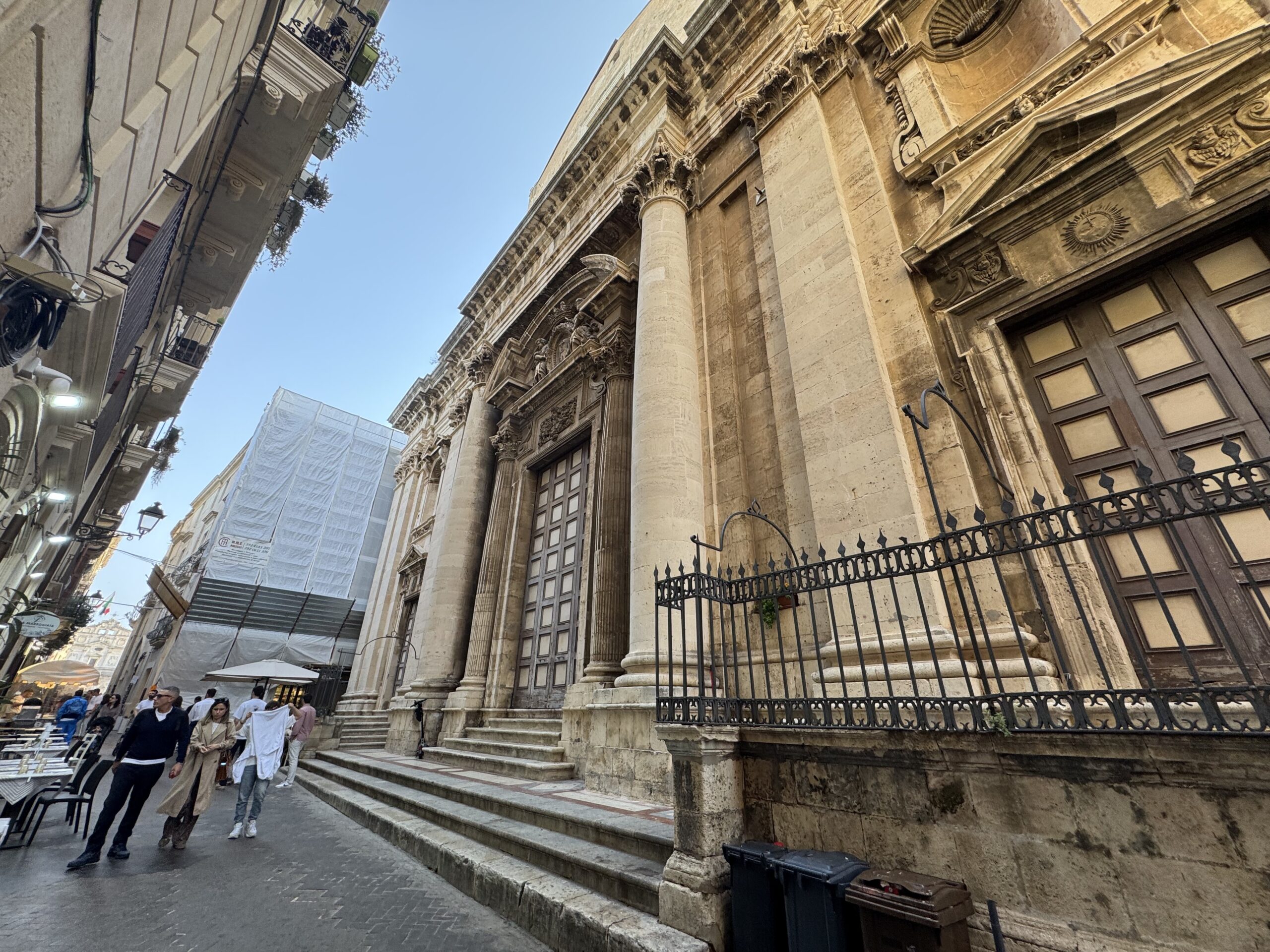 Vista contestuale della Chiesa del Collegio dei Gesuiti dalla stretta via Saverio Landolina con tavolini di ristoranti e passanti