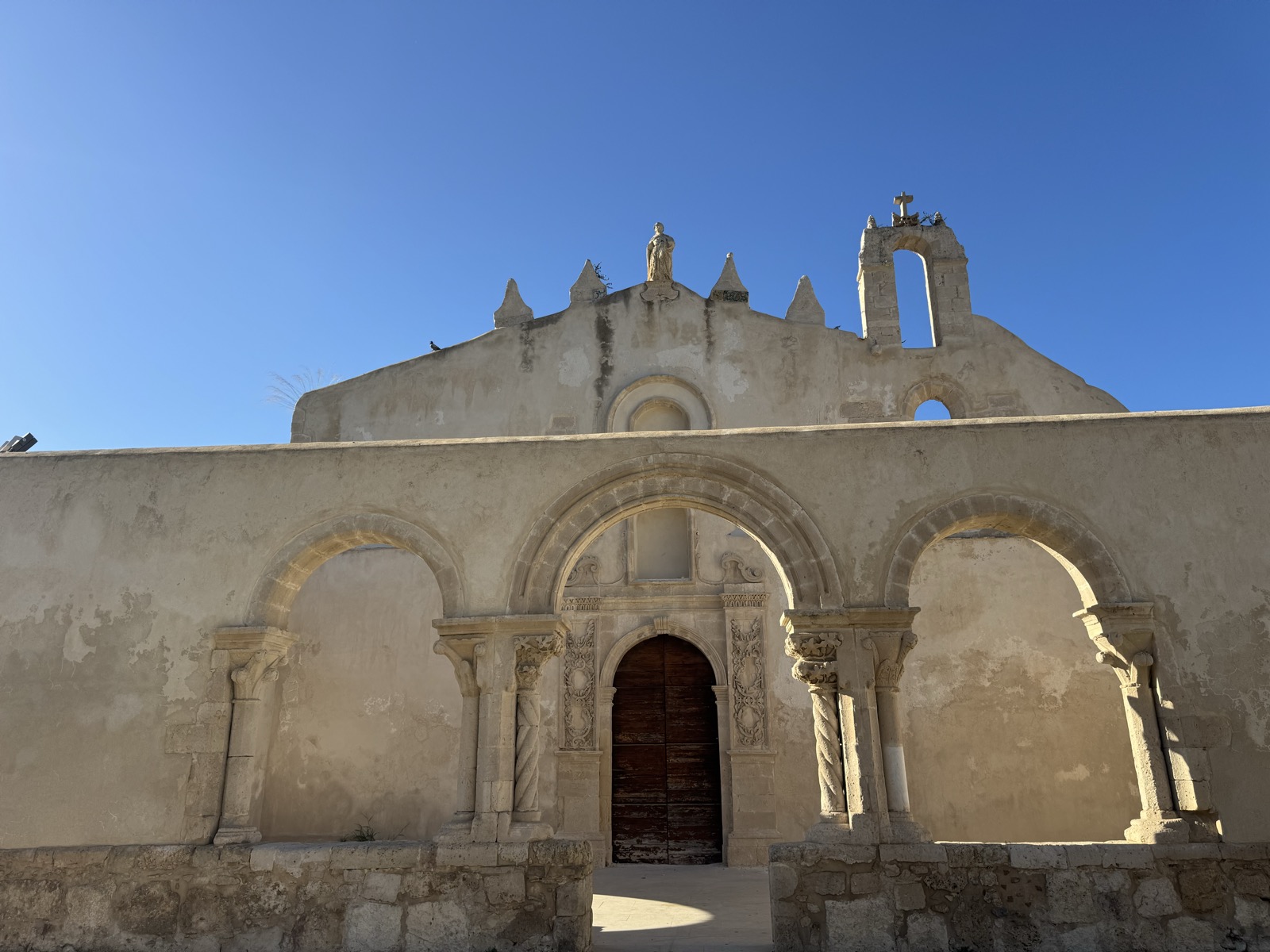 Dettaglio del portale con archi a sesto acuto della Chiesa di San Giovanni alle Catacombe a Siracusa: colonne tortili, capitelli scolpiti, arcate ogivali del portico di reimpiego.