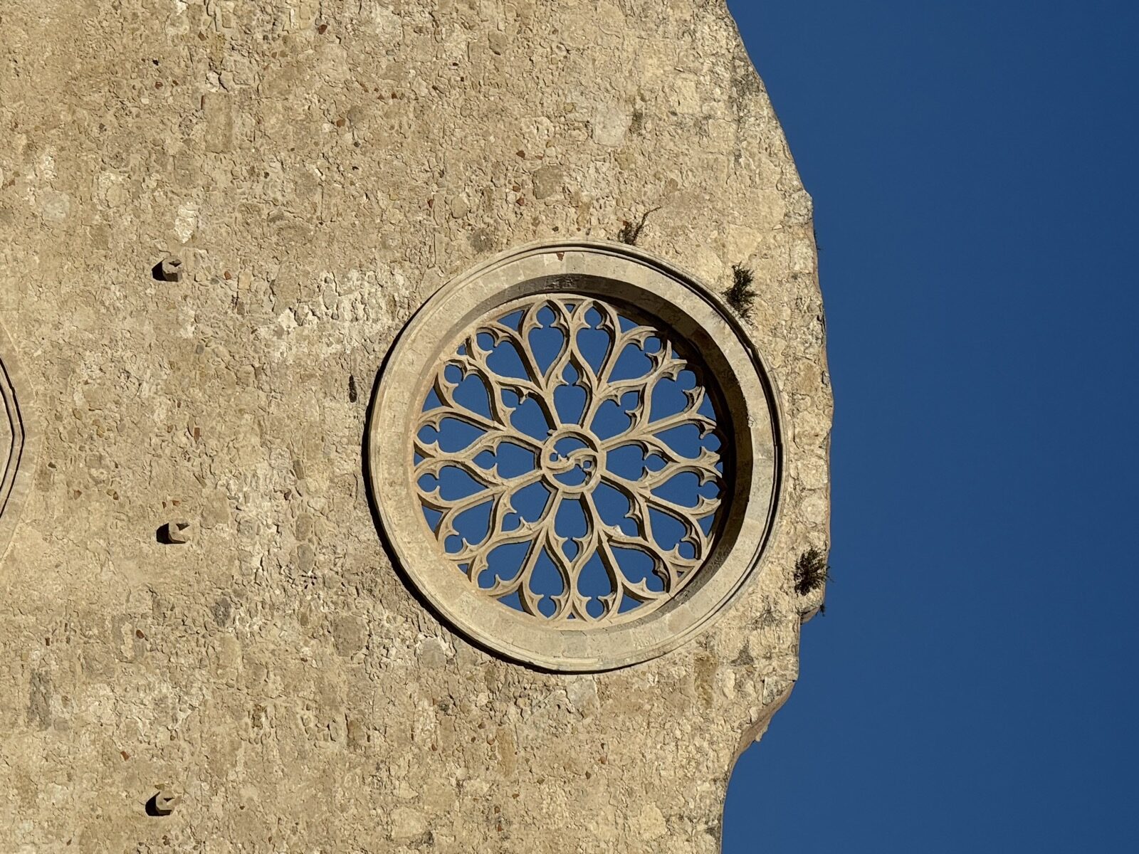 Dettaglio ravvicinato del rosone gotico-chiaramontano della Chiesa di San Giovanni alle Catacombe: traforo in pietra calcarea con petali cuoriformi disposti a raggera.
