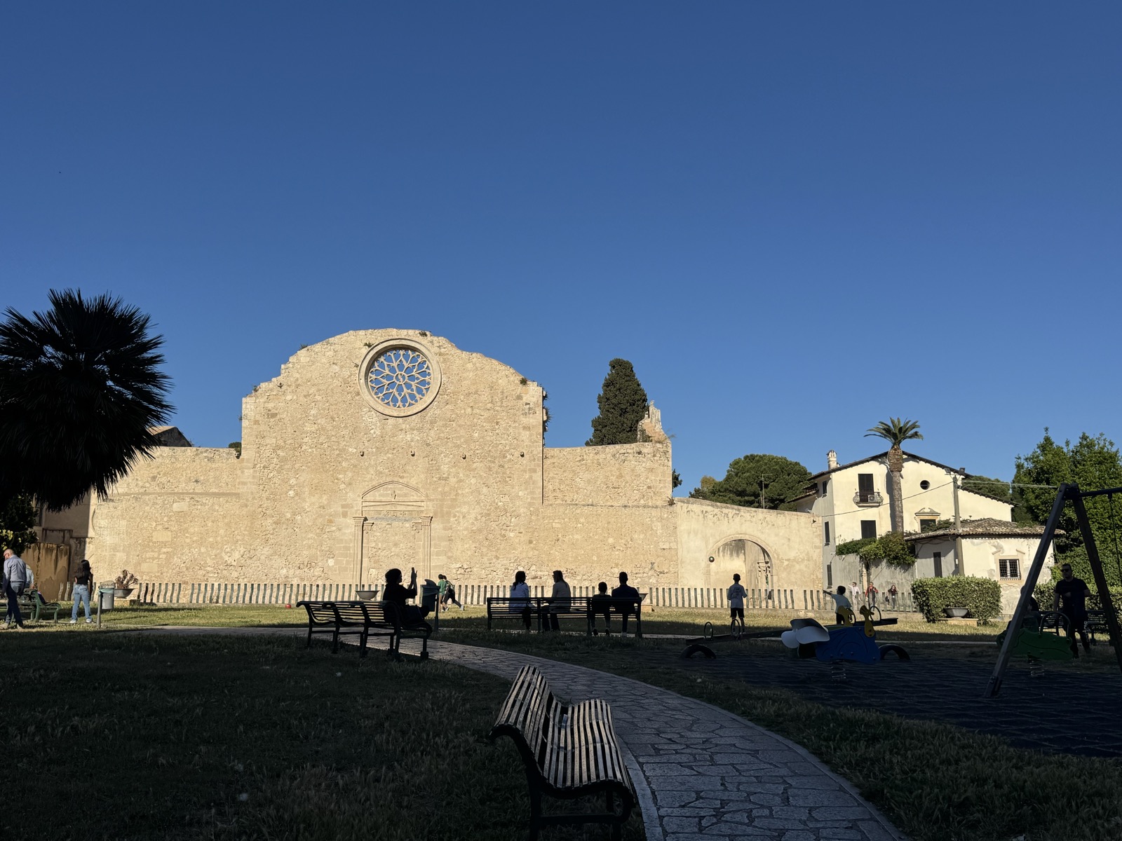 Vista posteriore della Chiesa di San Giovanni alle Catacombe dal parco antistante, con il grande rosone gotico-chiaramontano in primo piano sulla facciata.