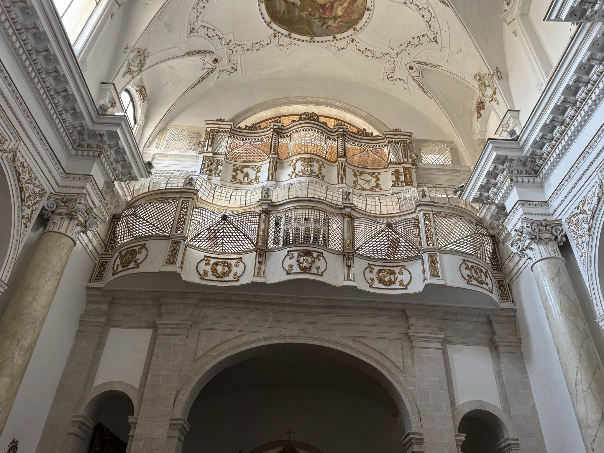 Cantoria sopraelevata in controfacciata, in legno e stucco bianco con decori dorati, mosse a tre arcate concave-convesse e custodia dell'organo a canne.