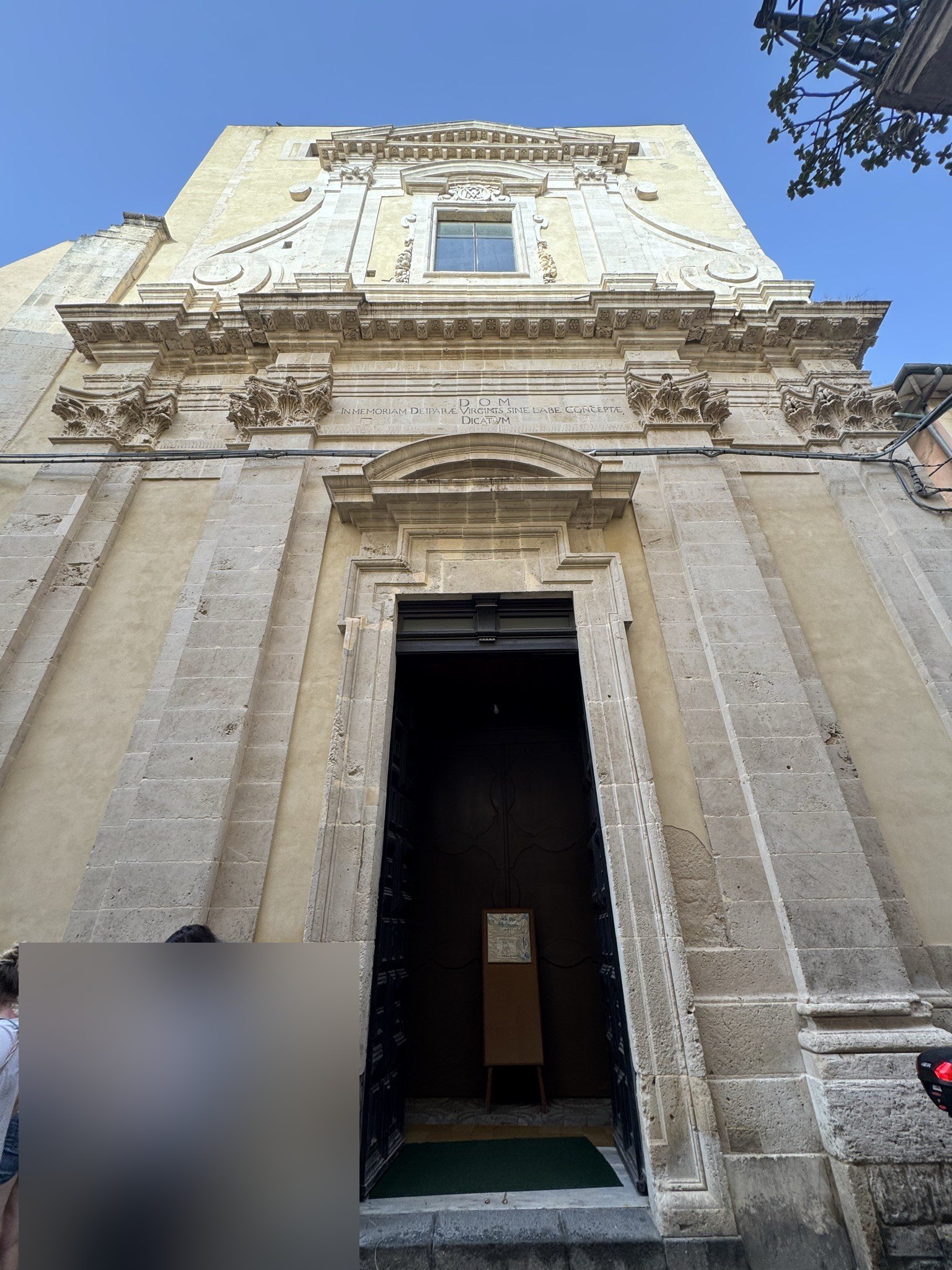 Facciata della chiesa vista dal basso: portale architravato, epigrafe del 1749, finestrone centrale e coronamento mosso a volute laterali.