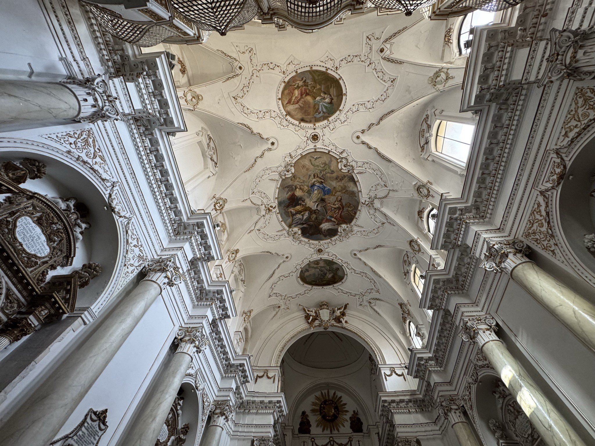 Volta a botte unghiata della chiesa con riquadri affrescati a colori e medaglioni in stucco bianco, raffiguranti la gloria mariana e scene allegoriche.