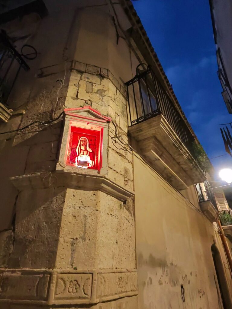 Vista architettonica notturna del cantonale con l'edicola illuminata di rosso e il lampione stradale