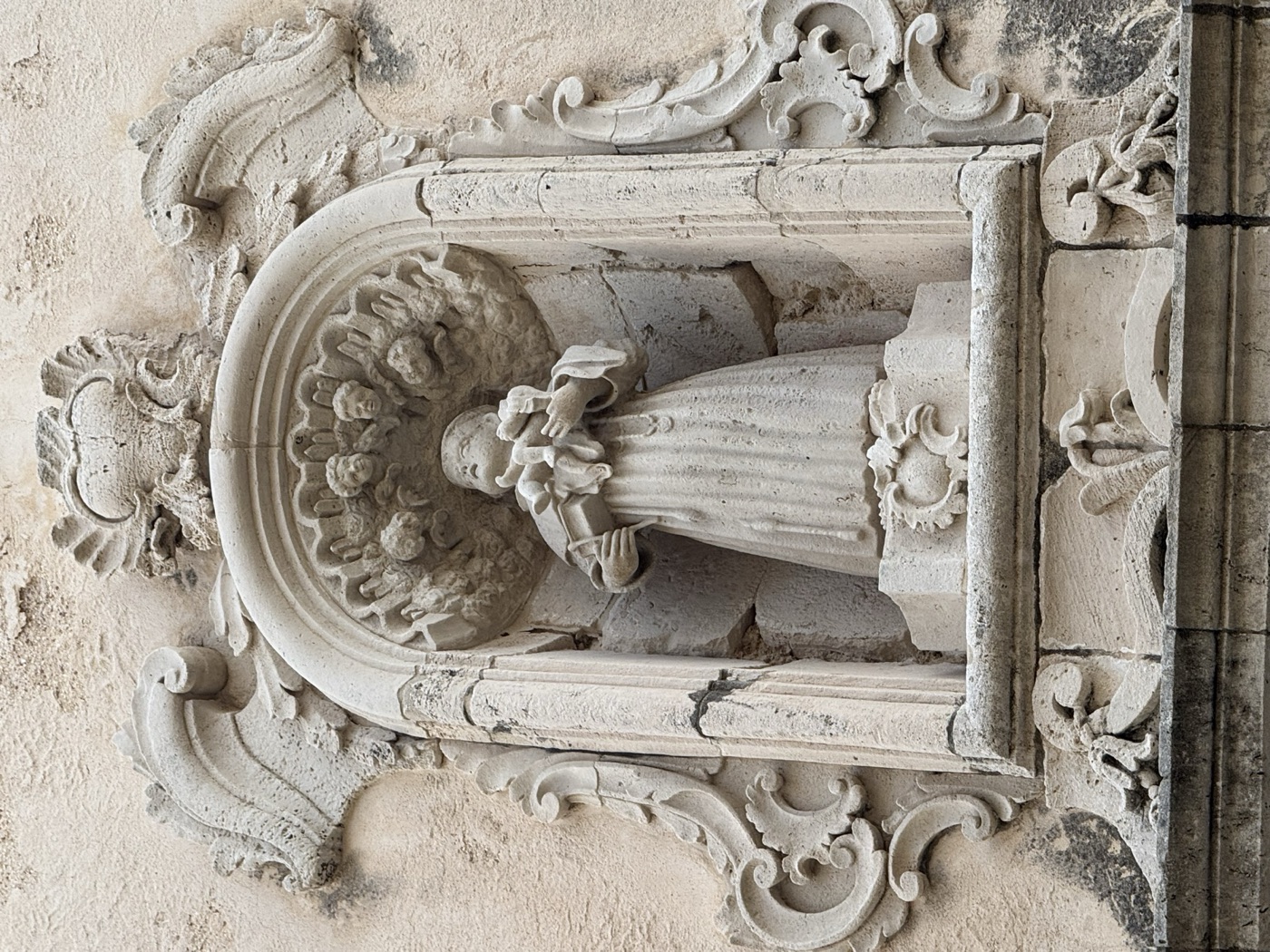 Dettaglio del Bambino Gesù in braccio a Sant'Antonio di Padova nella statua in pietra calcarea dell'edicola di via Vittorio Veneto 41 Ortigia
