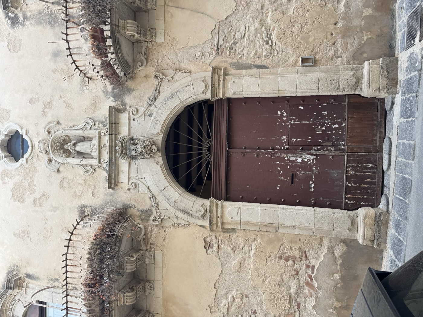 Vista del portone principale del palazzo di via Vittorio Veneto 41 Ortigia con bugnato in pietra e edicola votiva di Sant'Antonio di Padova visibile in alto in scorcio
