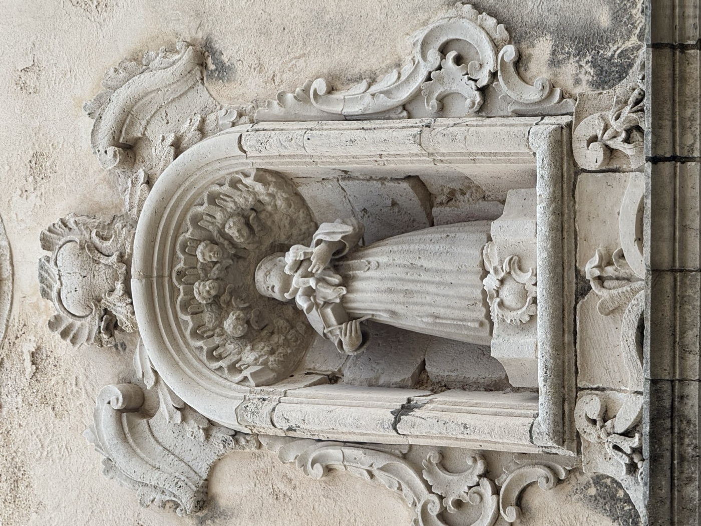 Dettaglio ravvicinato della statua in pietra calcarea di Sant'Antonio di Padova col Bambino nell'edicola di Palazzo Mezio-Blanco, via Vittorio Veneto 41 Ortigia, con saio francescano, Bambino Gesù in braccio e volta a conchiglia di sfondo nella nicchia ovale