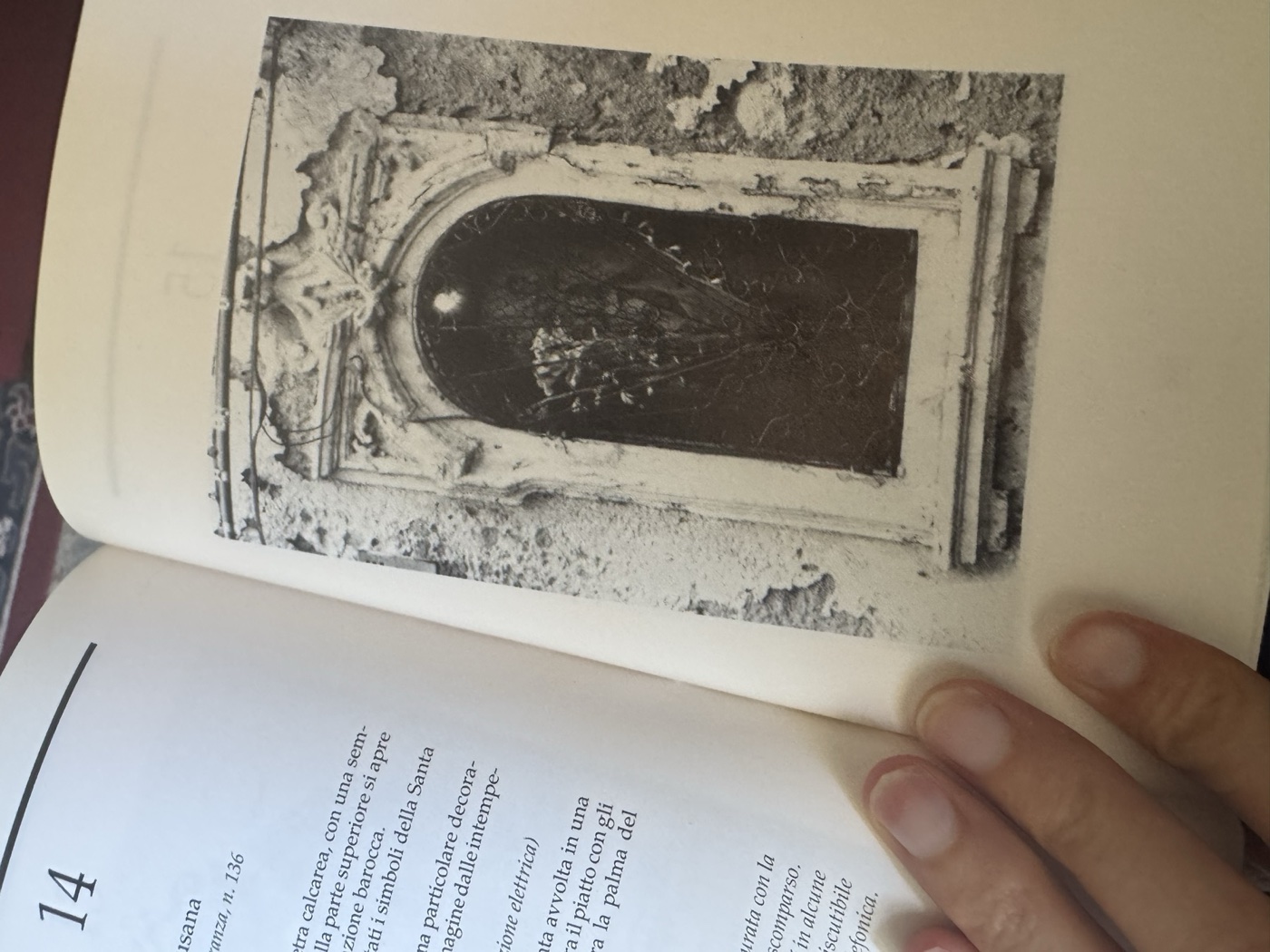 Fotografia in bianco e nero pubblicata da Michele Romano nel 1991 dell'edicola di Santa Lucia in via della Maestranza 136, con pietra calcarea degradata, sportello in ferro battuto a raggiera, dipinto su tavola con pellicola pittorica che si solleva e garofani rossi all'interno