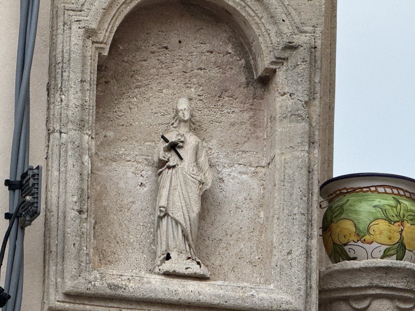 Dettaglio della statua scolpita in pietra calcarea di Santa Lucia con veste drappeggiata e palma del martirio nelledicola del cantonale piazzetta San Rocco via Picherali Ortigia