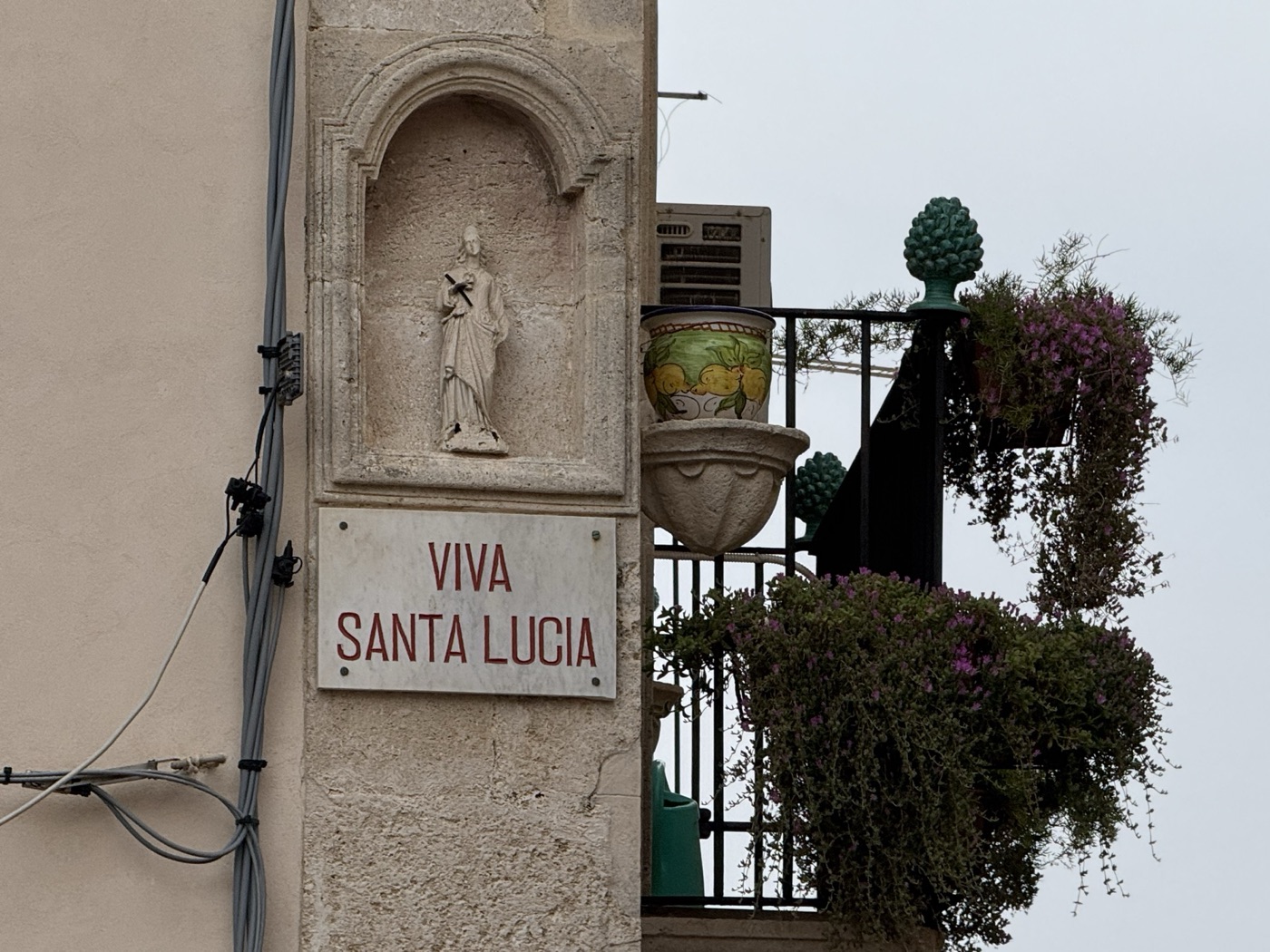 Vista dell'edicola di Santa Lucia nel cantonale piazzetta San Rocco via Picherali Ortigia con balcone vicino, pigna in ceramica siciliana di Caltagirone e pianta fiorita