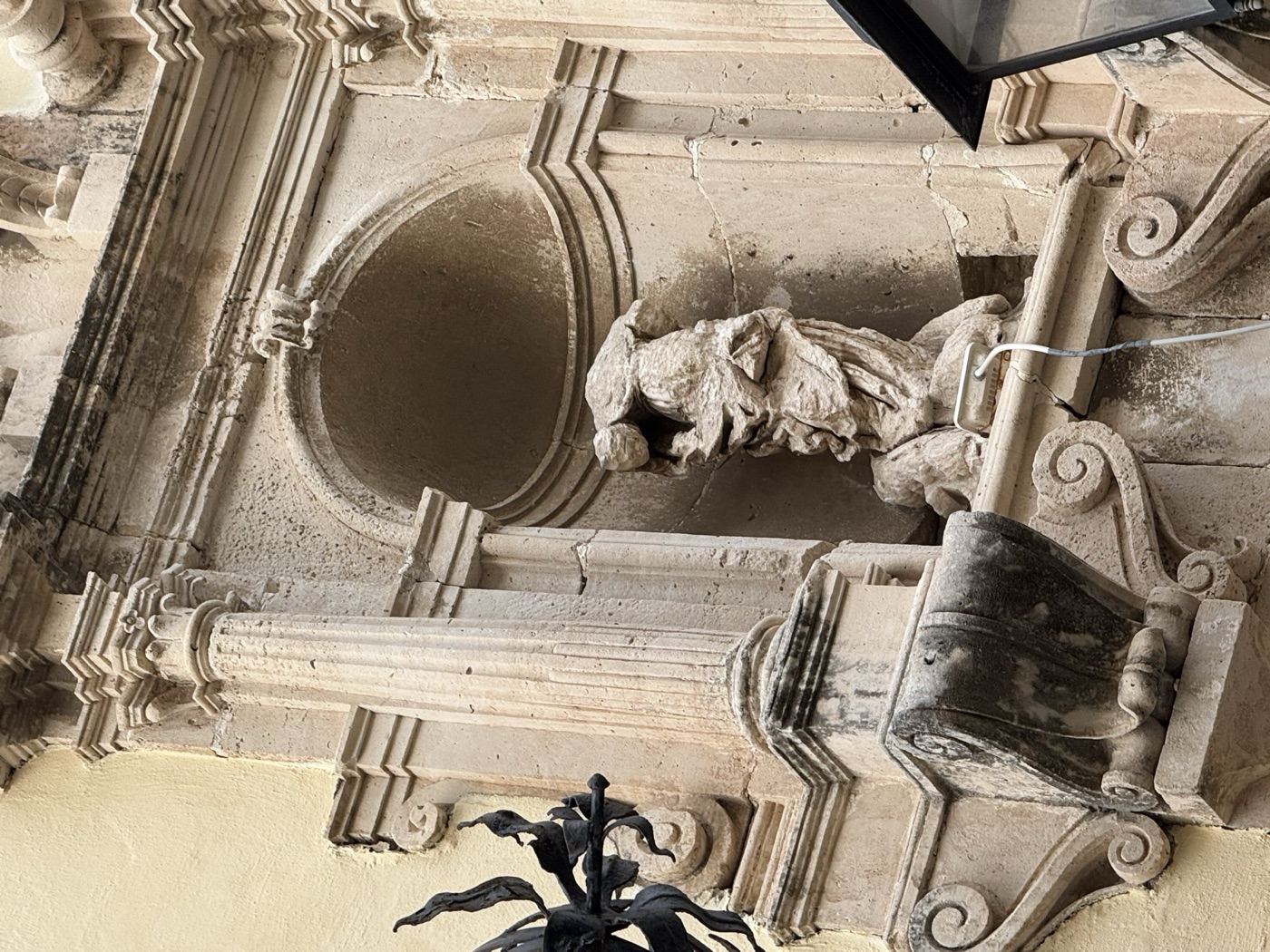 Dettaglio della parte inferiore dell'edicola di Santa Lucia su Palazzo Russo, con la base modanata della nicchia ovale, la statua acefala vista dall'alto e i segni di degrado della pietra