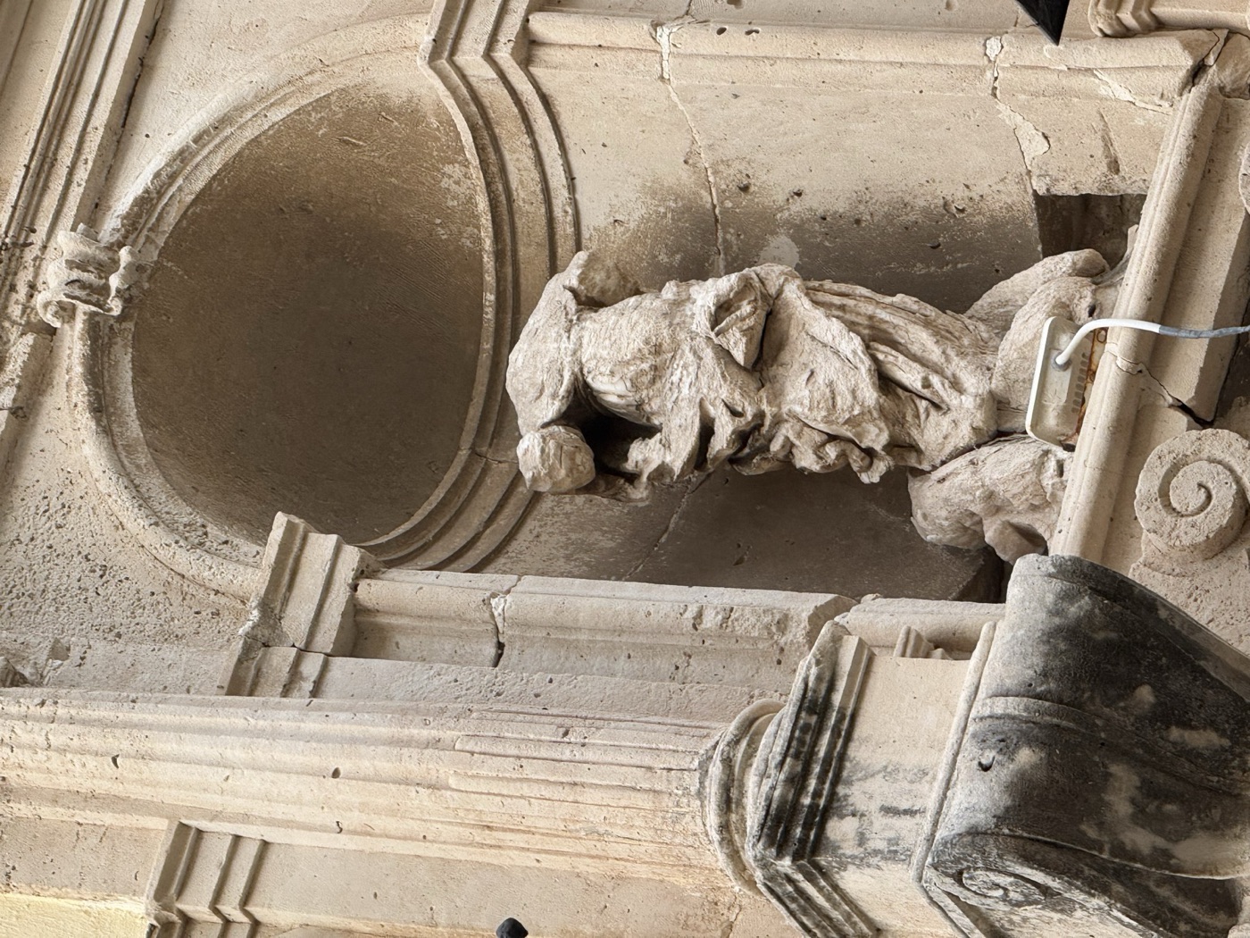 Dettaglio ravvicinato della statua acefala di Santa Lucia in pietra calcarea nell'edicola di Palazzo Russo, via Vittorio Veneto 22, Ortigia, con drappeggio della veste a vortice e mutilazione delle braccia visibili