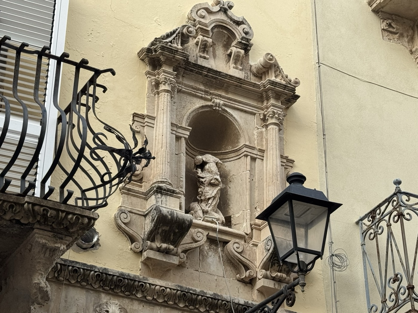 Vista frontale completa dell'edicola tardobarocca di Santa Lucia in pietra calcarea sul prospetto di Palazzo Russo, via Vittorio Veneto 22, Ortigia, con lampada votiva pendula e balcone in ferro battuto a sinistra