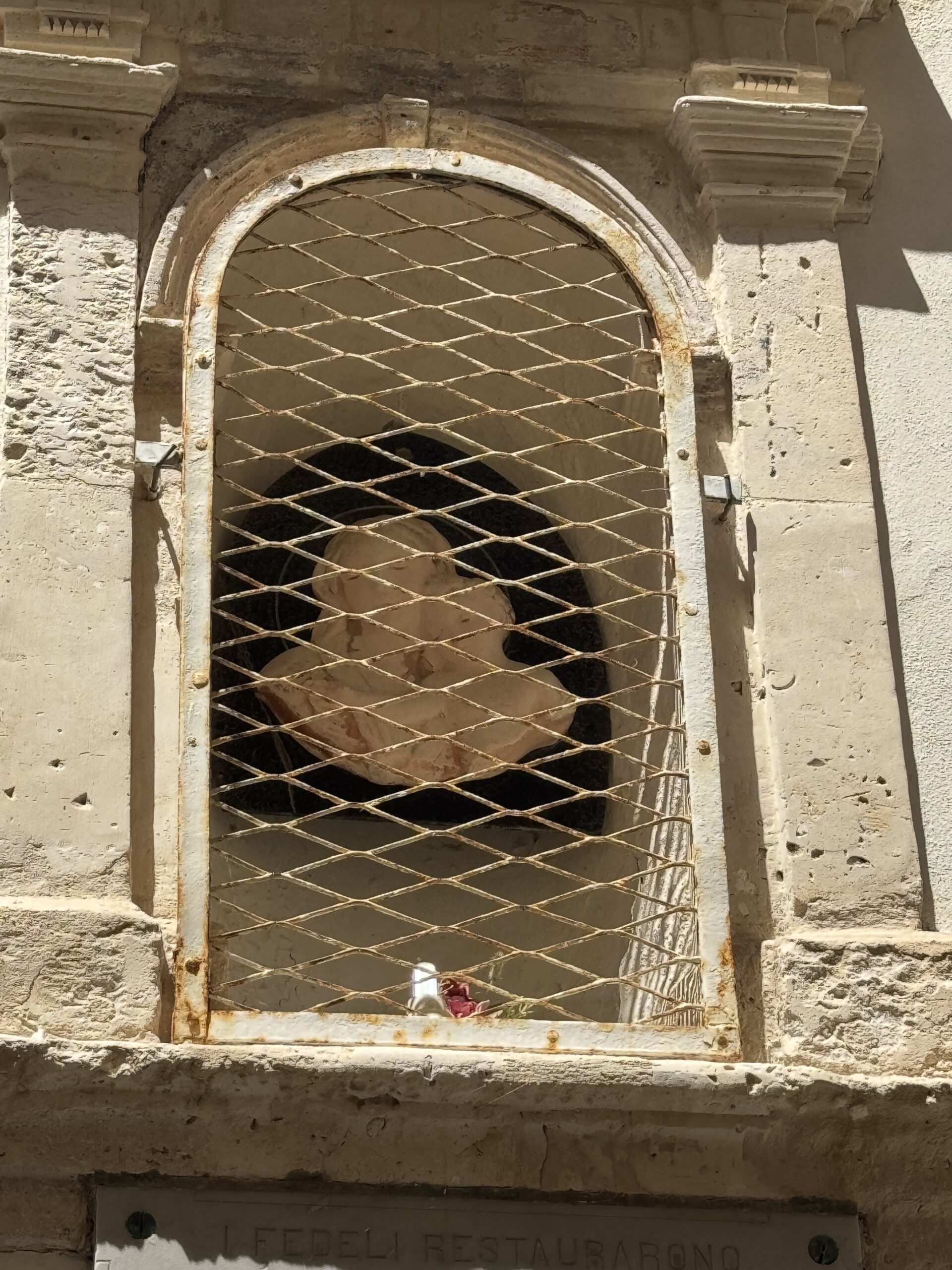 Nicchia ad arco con grata metallica a maglie romboidali e, all'interno, l'immagine mariana oggi molto degradata.