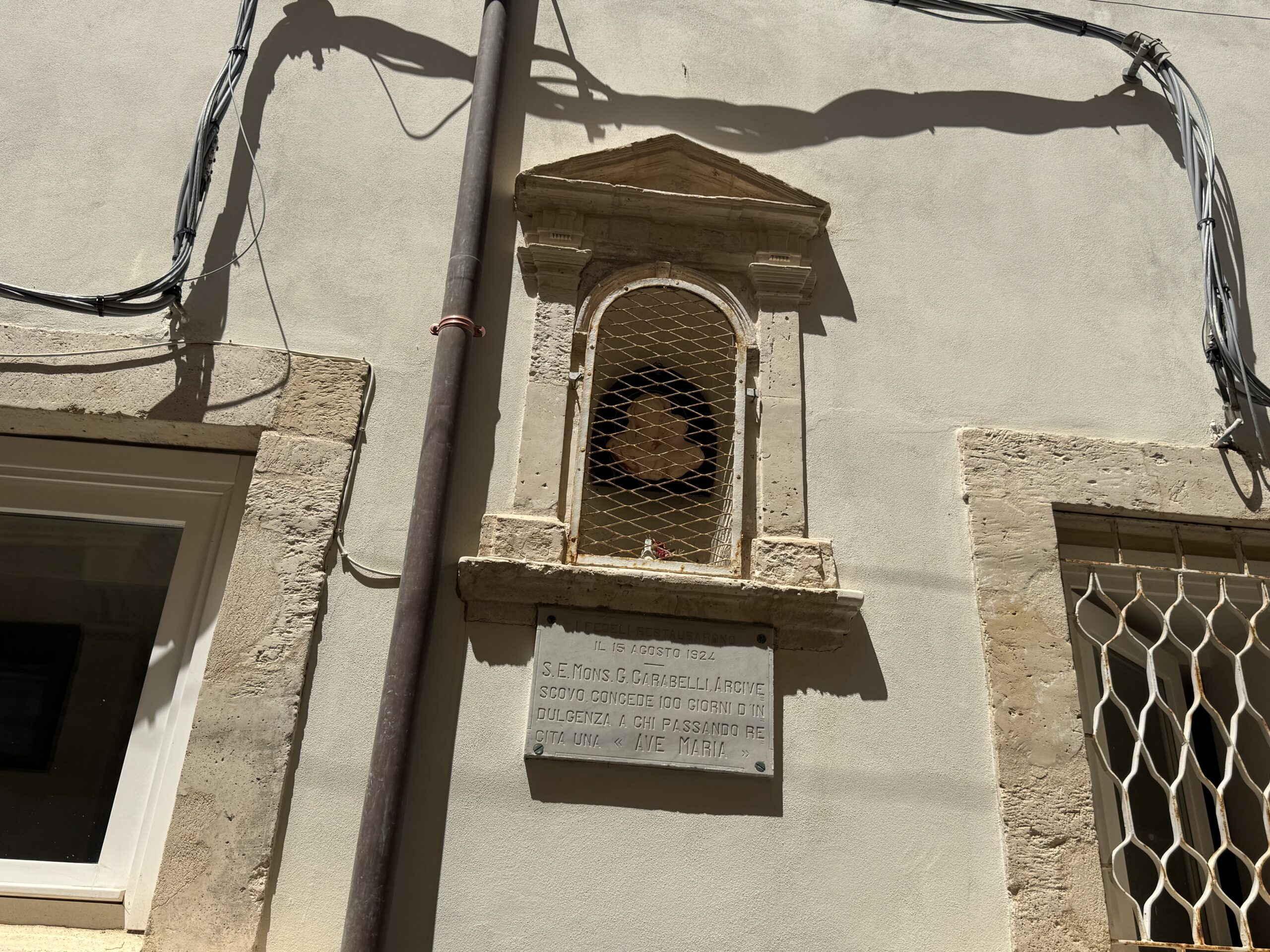 Facciata di una casa lungo un vicolo di Ortigia con l'edicola votiva incassata nel muro fra le finestre.