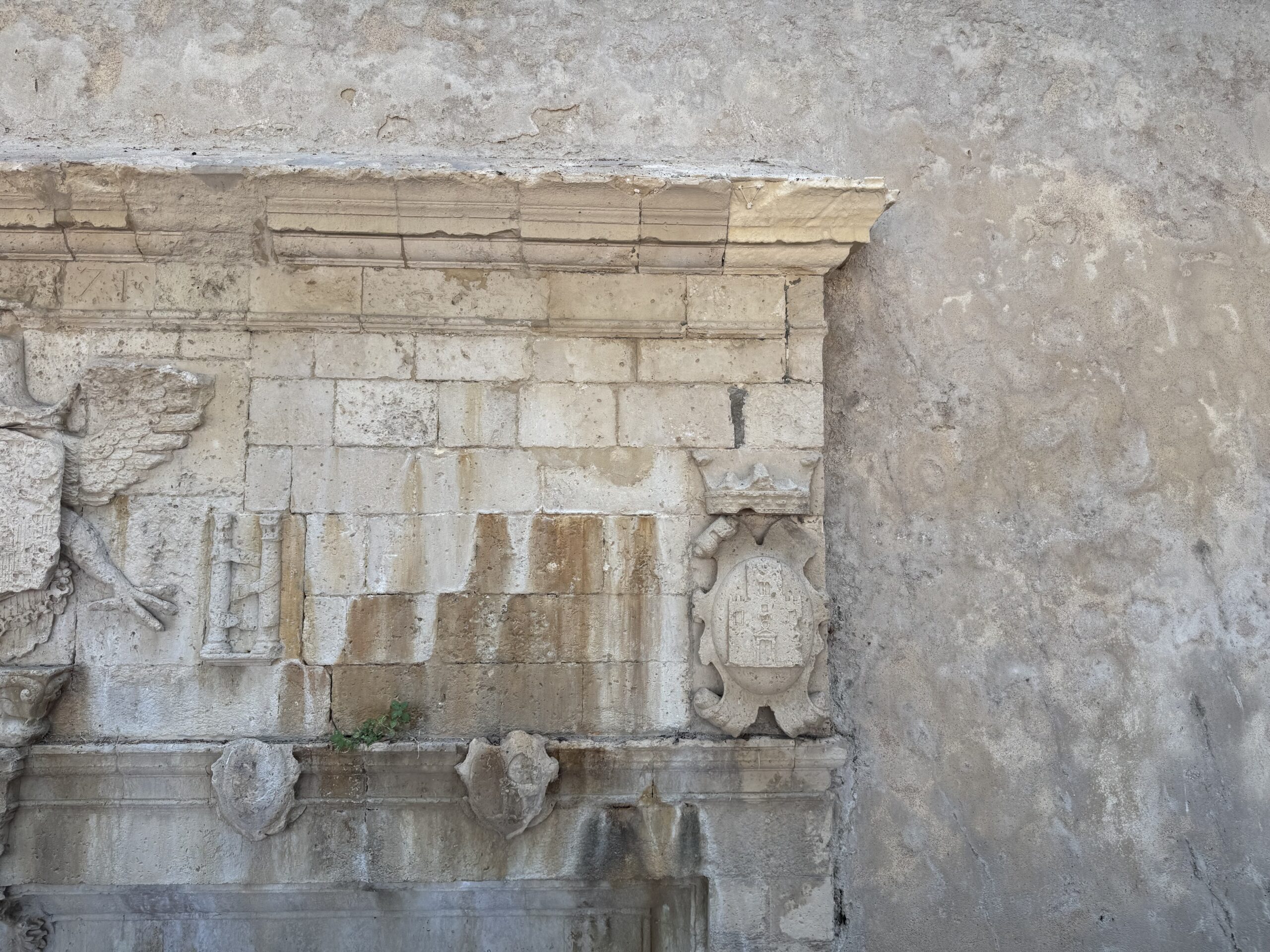 Particolare del prospetto della Fontana degli Schiavi con cornice aggettante, figure scolpite e stemmi araldici nella pietra calcarea.