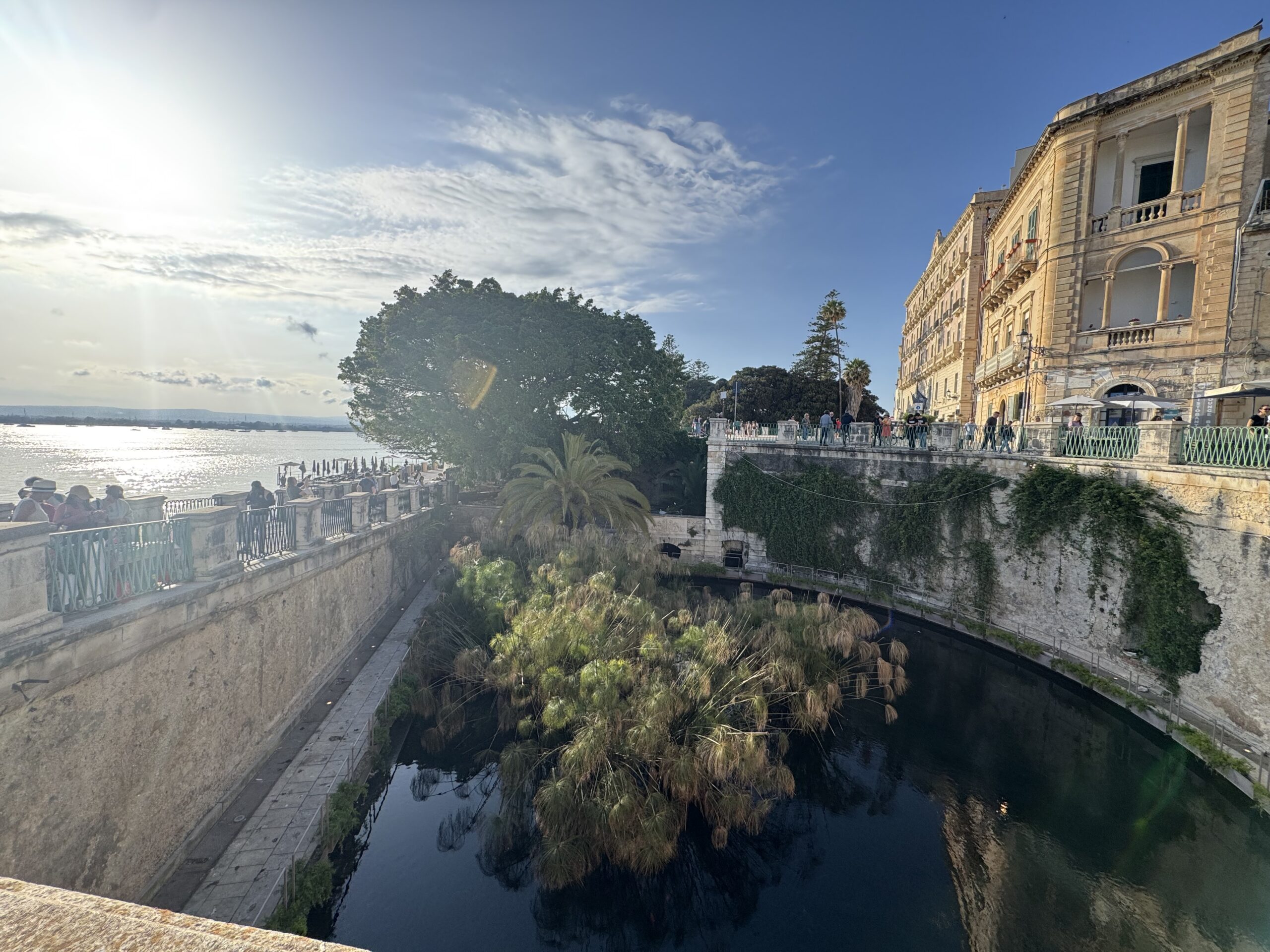 Vista d'angolo della Fonte Aretusa con la balaustra del belvedere che incontra il mare aperto.