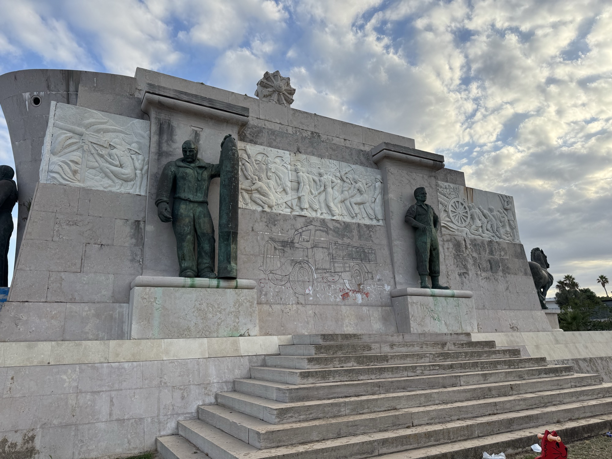 Lato del monumento con le statue bronzee del marinaio e dell'aviatore e i bassorilievi del lavoro coloniale