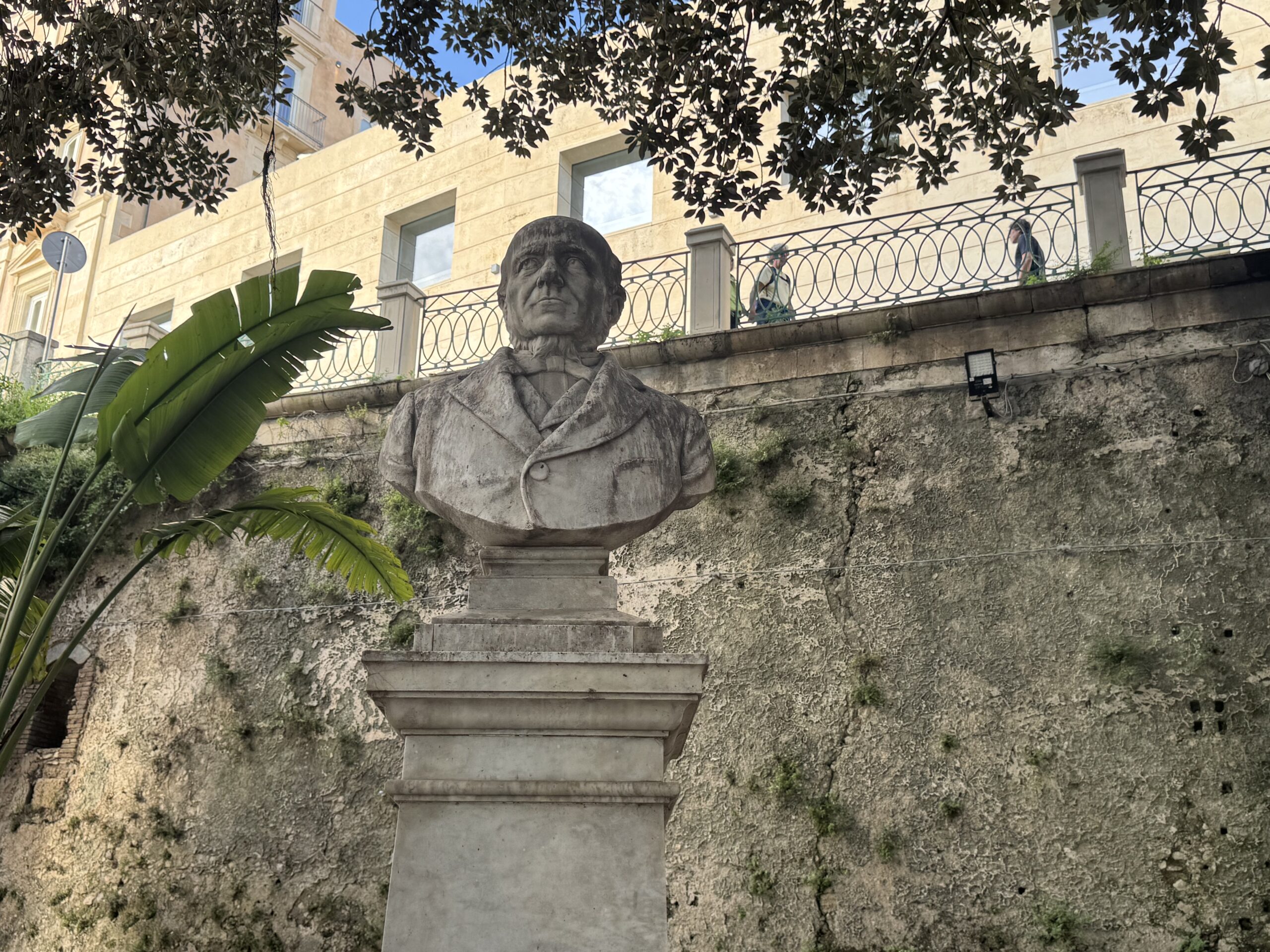 Dettaglio del busto in pietra di Carmelo Campisi: volto naturalistico con barba e baffi, redingote a doppio petto, cravatta annodata.