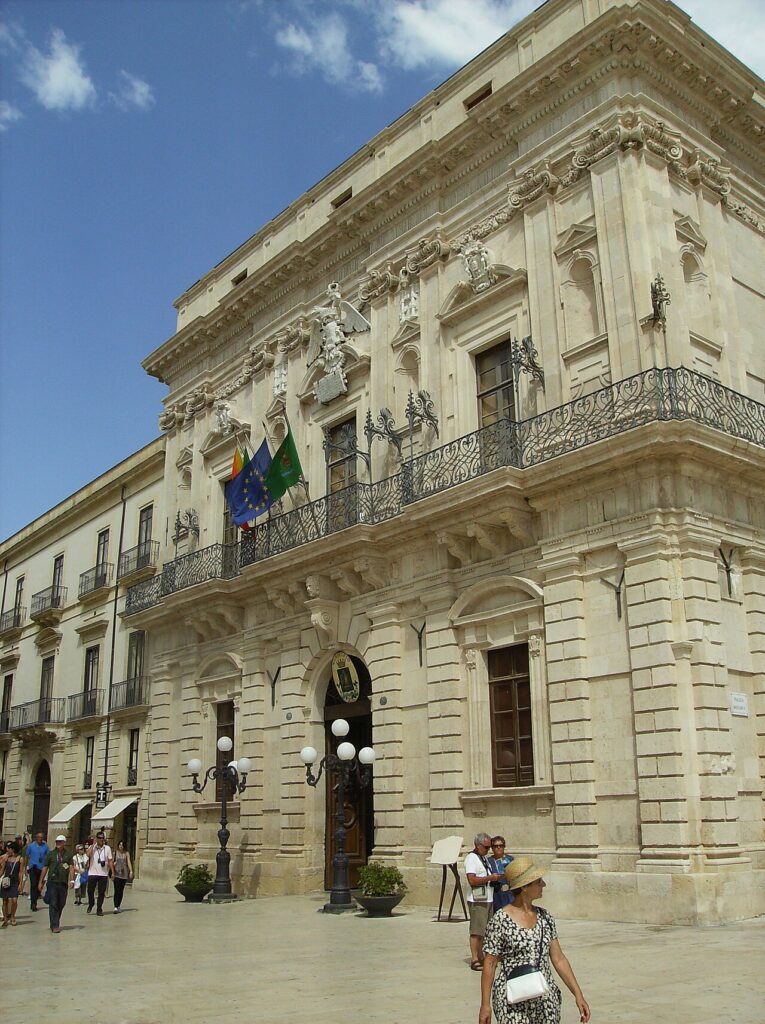 Edificio storico con balcone in ferro battuto e bandiere.