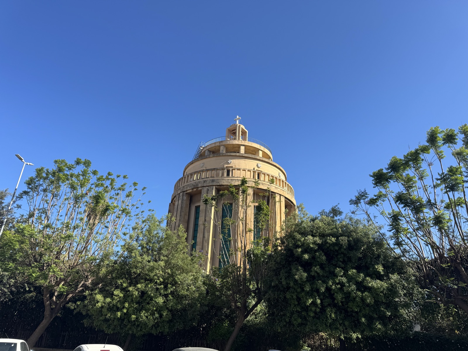 Vista frontale del Pantheon dei Caduti dal basso, con vegetazione del piazzale in primo piano e cielo limpido.